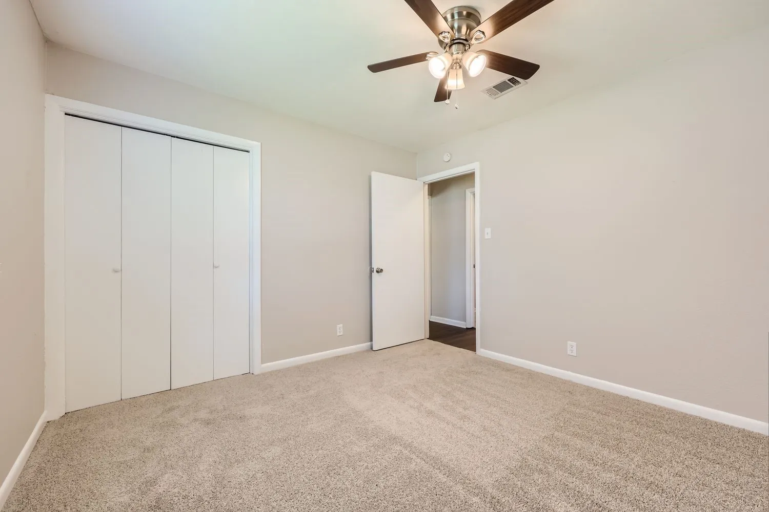 Carpeted room featuring a ceiling fan with light fixture, neutral wall color, white baseboards, and a bi-fold closet