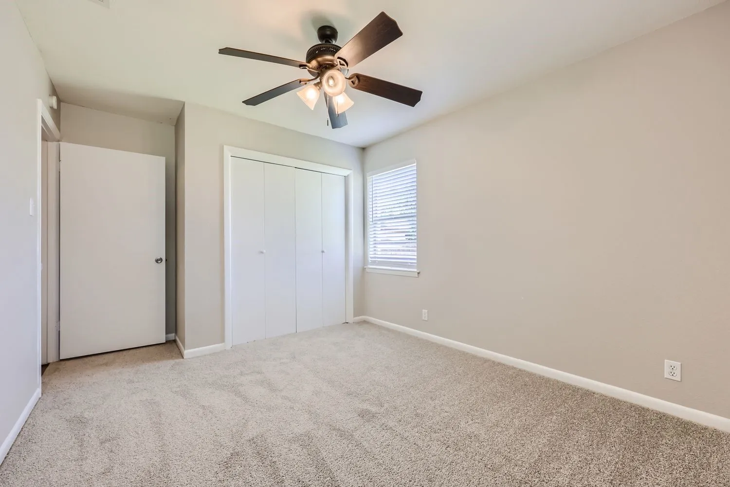 Carpeted room with neutral wall paint, a ceiling fan with light fixture, a window with horizontal blinds, and bi-fold closet doors