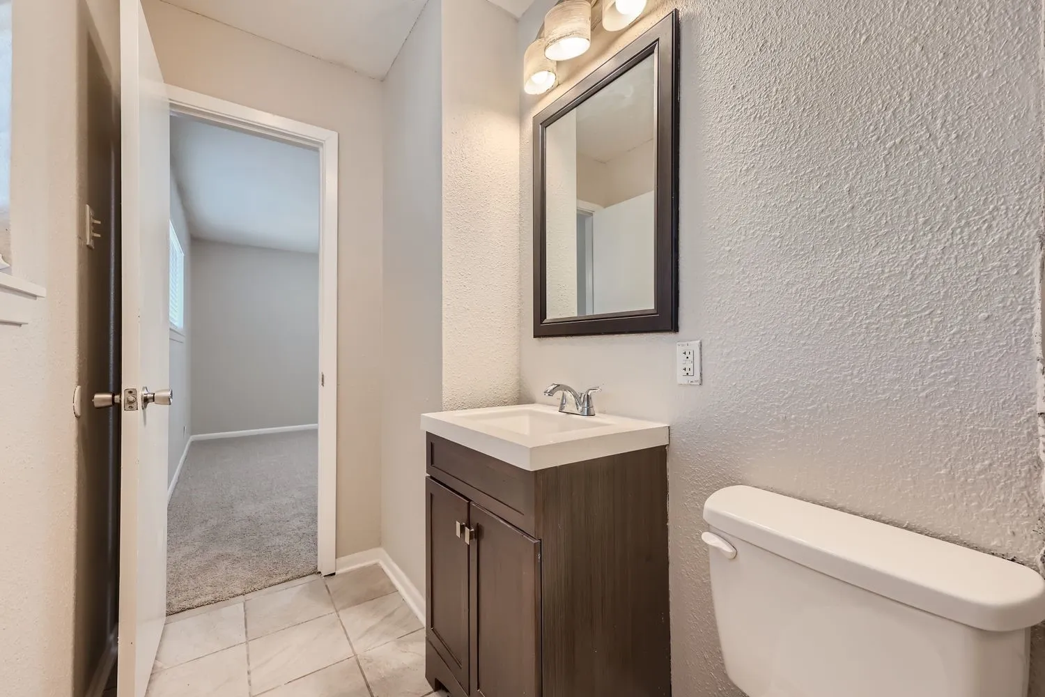Bathroom vanity featuring a dark wood-finish cabinet with white countertop, chrome faucet, and a rectangular mirror