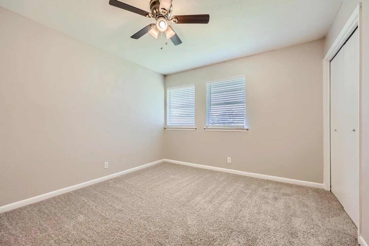 Spacious bedroom featuring neutral carpeting, dual windows with plantation shutters, ceiling fan with integrated lighting, and fresh neutral wall finishes