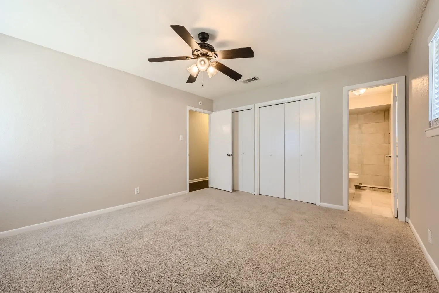 Carpeted room featuring a ceiling fan with integrated lighting, two bi-fold door closets, and a window with horizontal blinds