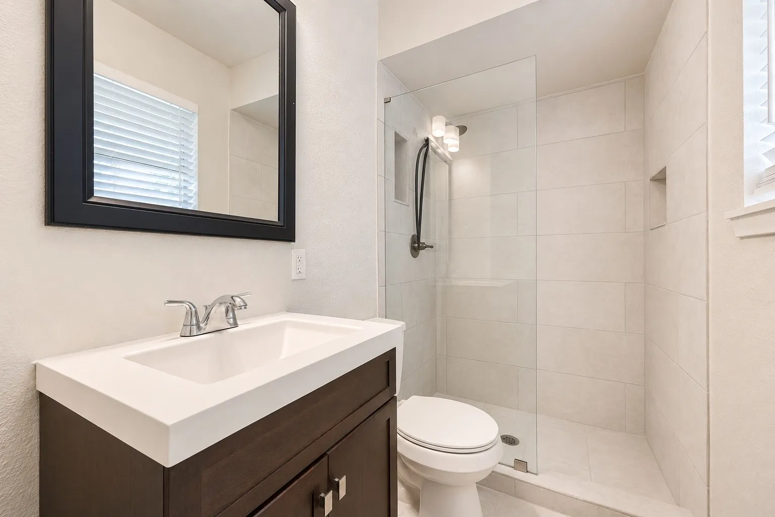 Modern bathroom featuring a dark wood-finish vanity with an integrated white sink and a frameless glass shower enclosure