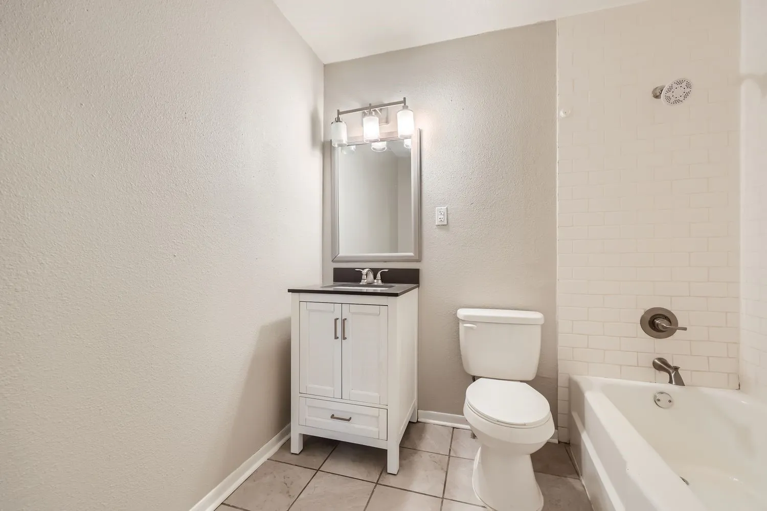 Bathroom featuring a white vanity with dark countertop, an overhead vanity light fixture, a toilet, and a bathtub with white subway tile surround