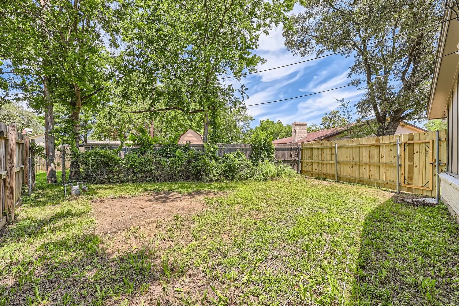 Expansive backyard featuring a combination of wood plank and chain link fencing, mature trees, and a wooden gate