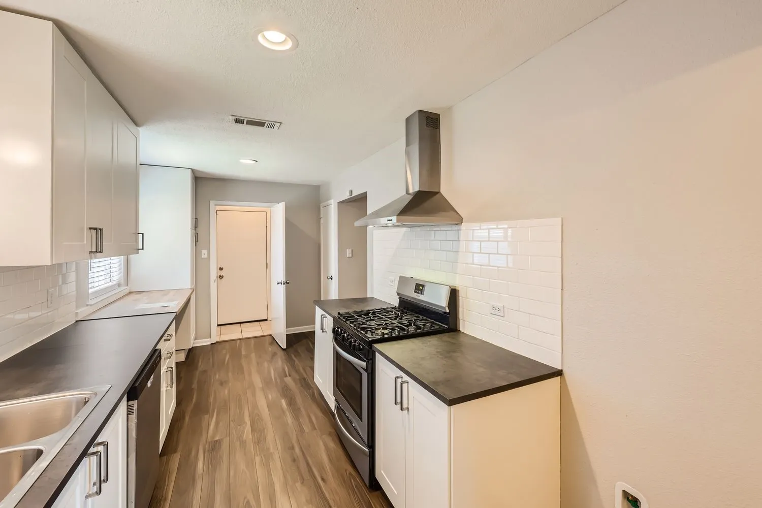 Modern kitchen featuring wood-finish flooring, white cabinetry with contemporary hardware, and dark countertops