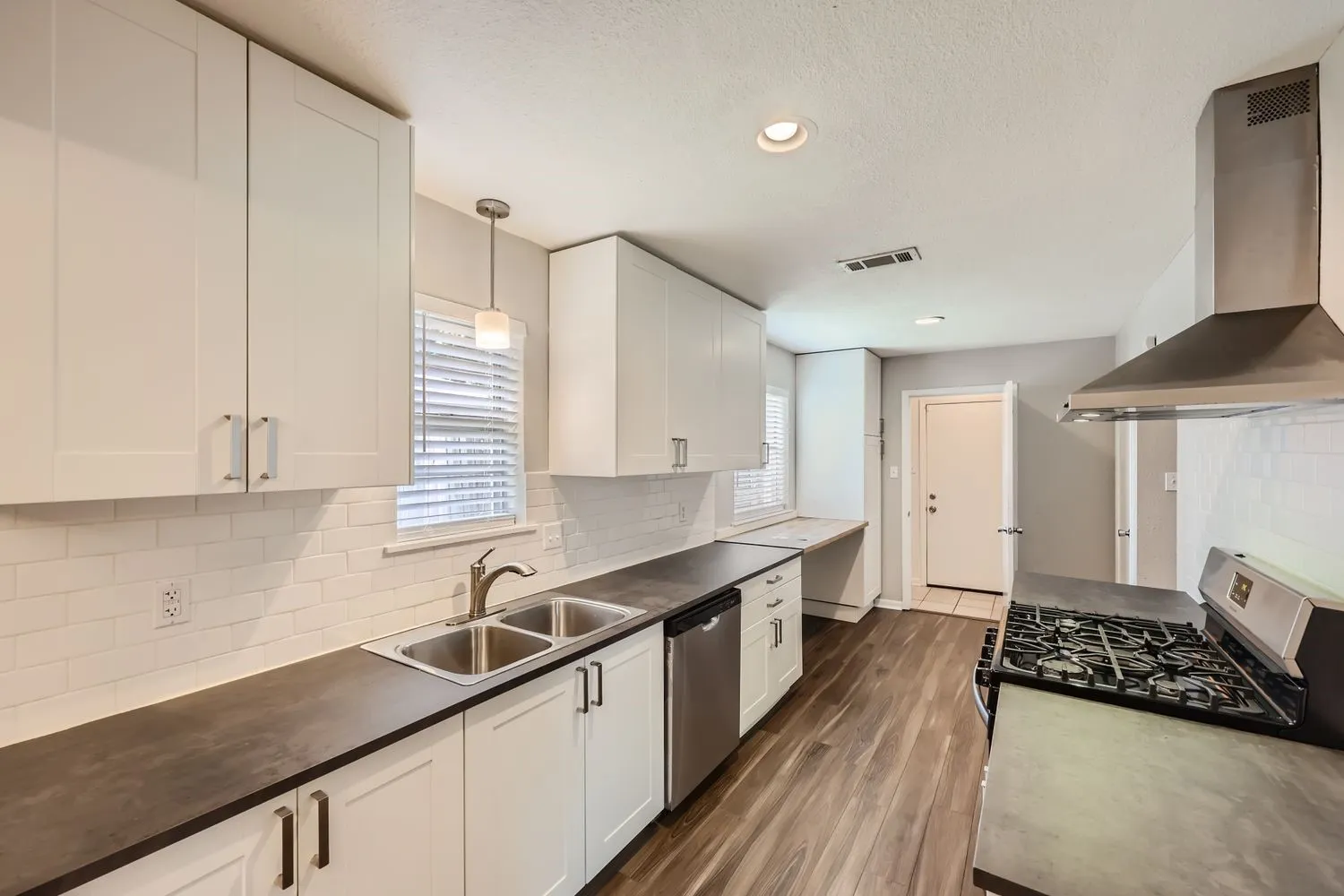 Modern kitchen featuring white shaker-style cabinetry, dark wood-finish countertops, subway tile backsplash, stainless steel appliances including a gas cooktop and range hood, and wood-finish flooring throughout