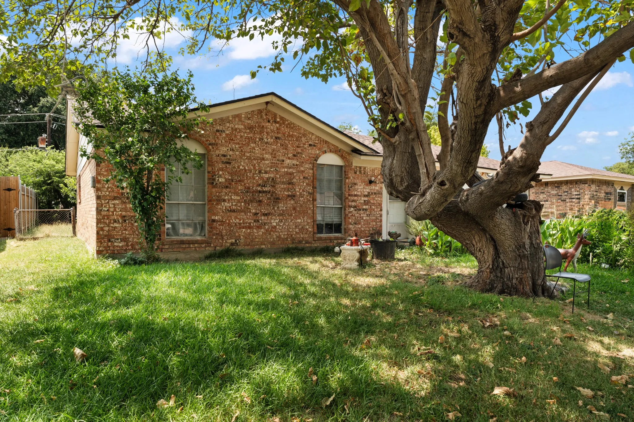 Brick exterior with an arched window, featuring a gabled roofline, mature trees, and a grassy lawn