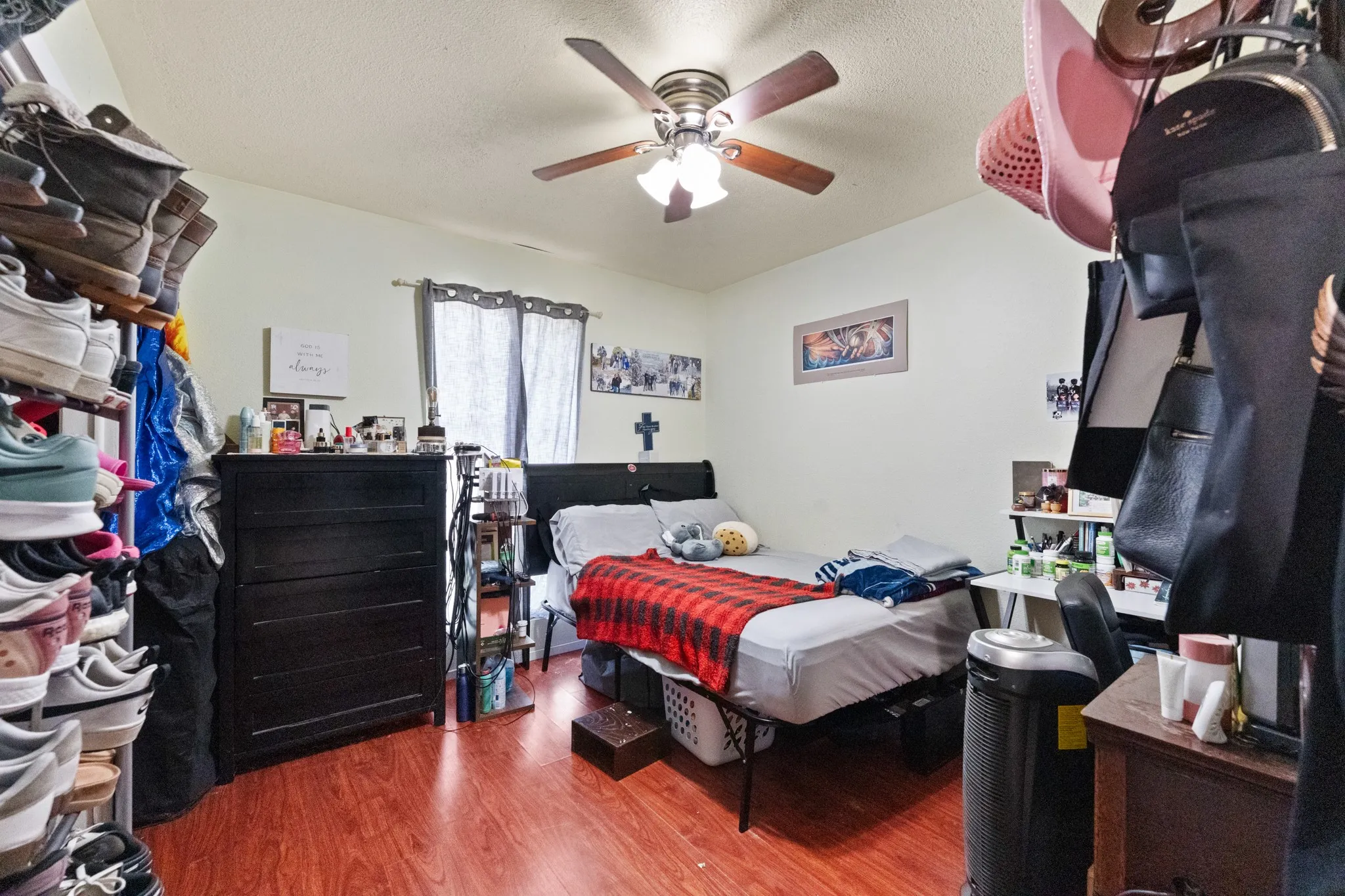 Bedroom featuring wood-finish flooring, a ceiling fan with light fixture, and window with dark curtains