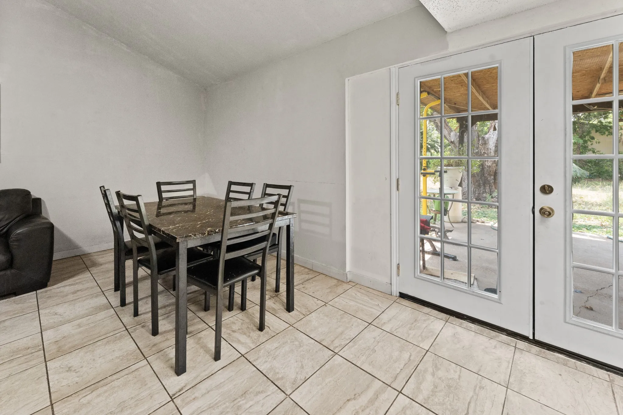 Bright dining area with tile flooring, round dining table with seating for four, and dual glass French doors opening to the exterior