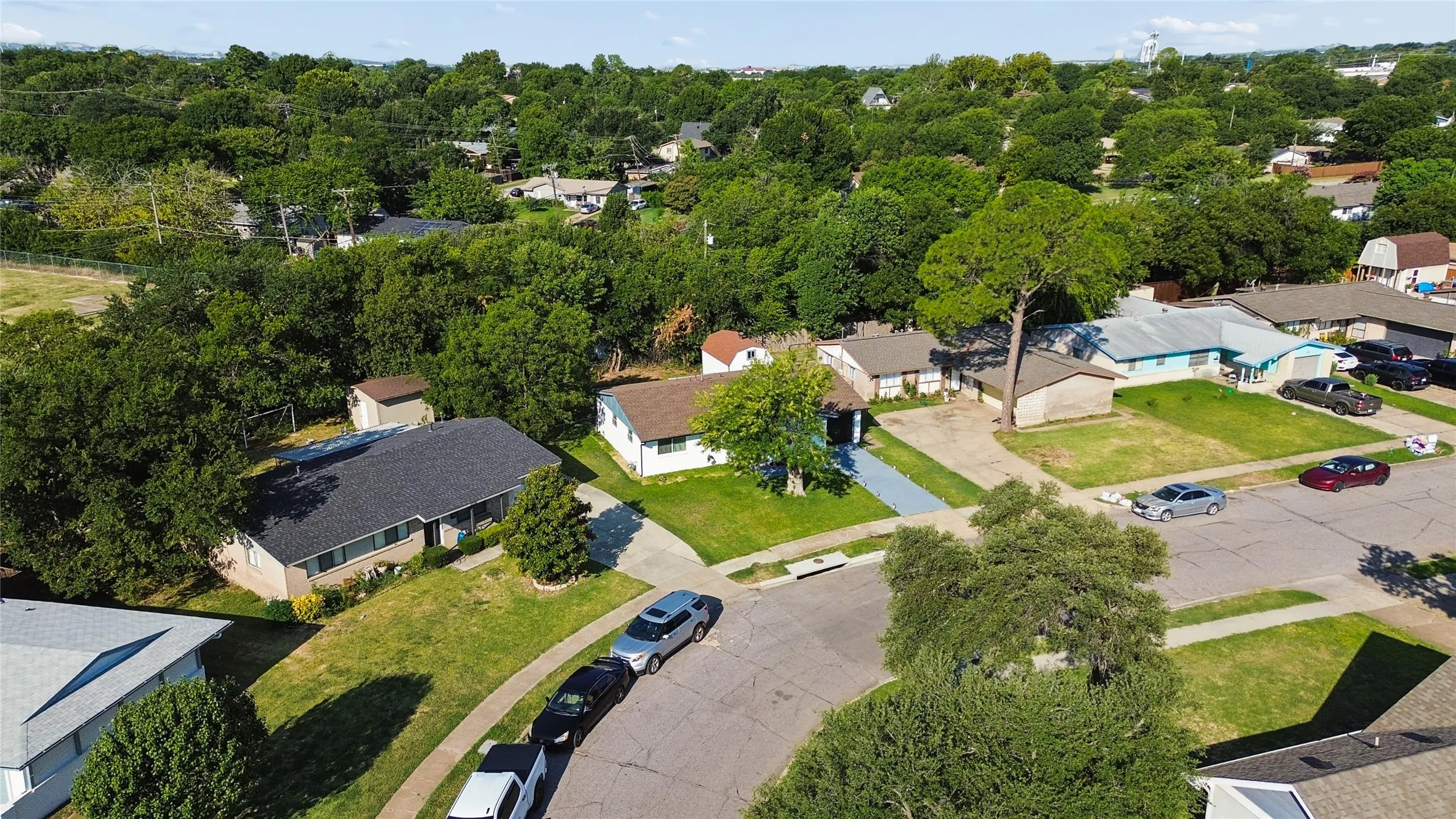 Aerial view showcasing a substantial corner lot with mature landscaping, manicured lawn, and established trees throughout the property