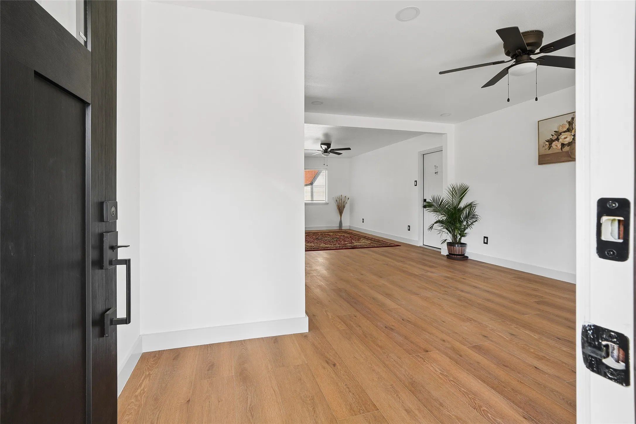 Entryway featuring light wood-finish flooring, white baseboards, and a modern dark-paneled door with matte black hardware