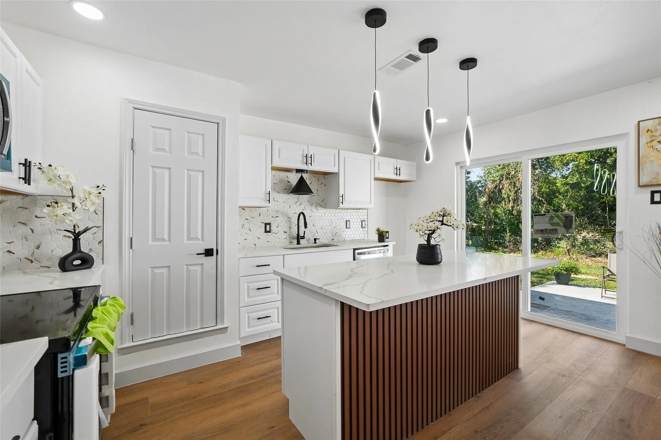 Modern kitchen featuring a central island with a slatted wood-finish base and light-toned countertop, white cabinetry with dark hardware, a patterned backsplash, and wood-finish flooring