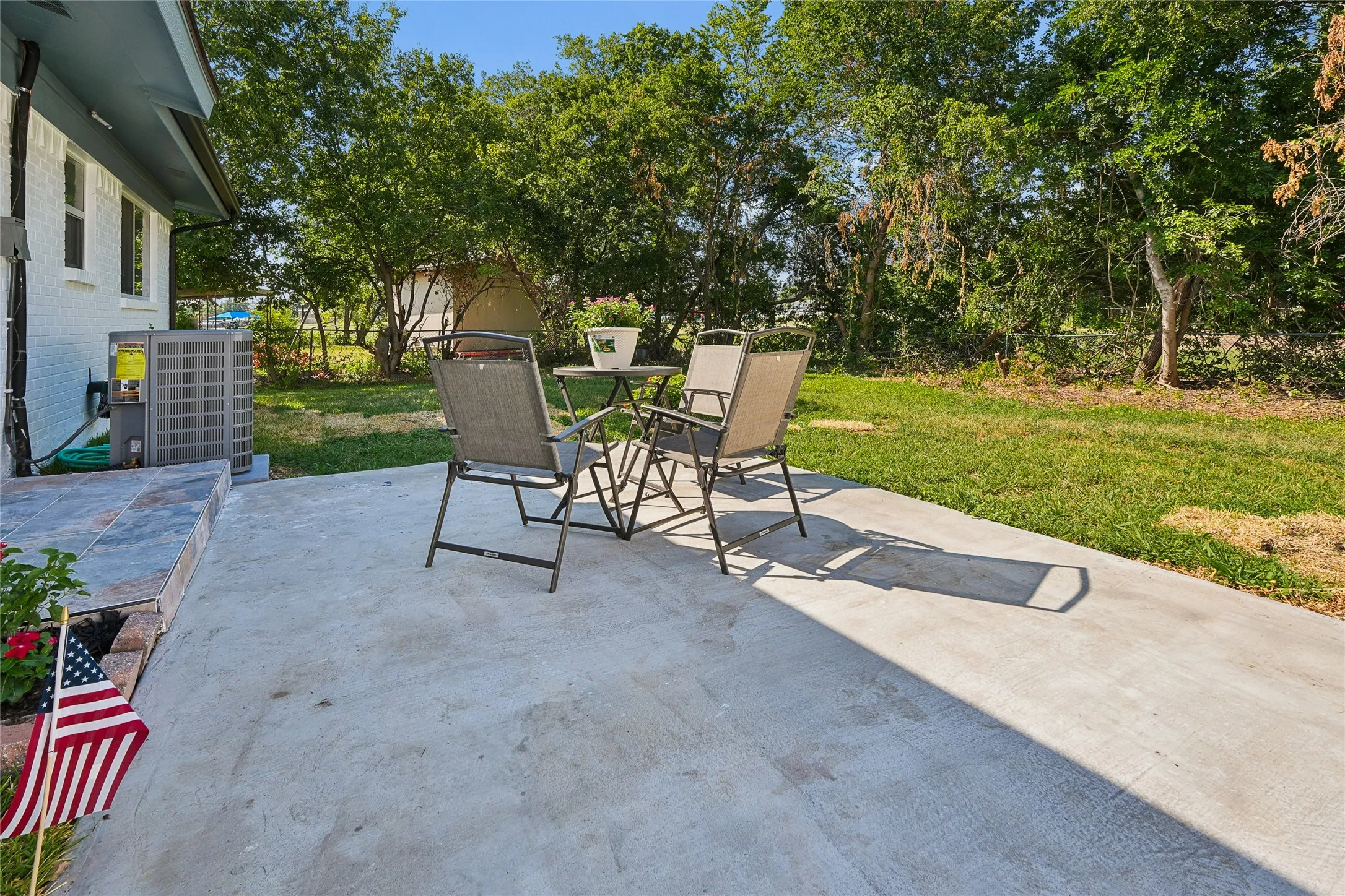Concrete patio with a tiled entry, expansive lawn, and mature trees