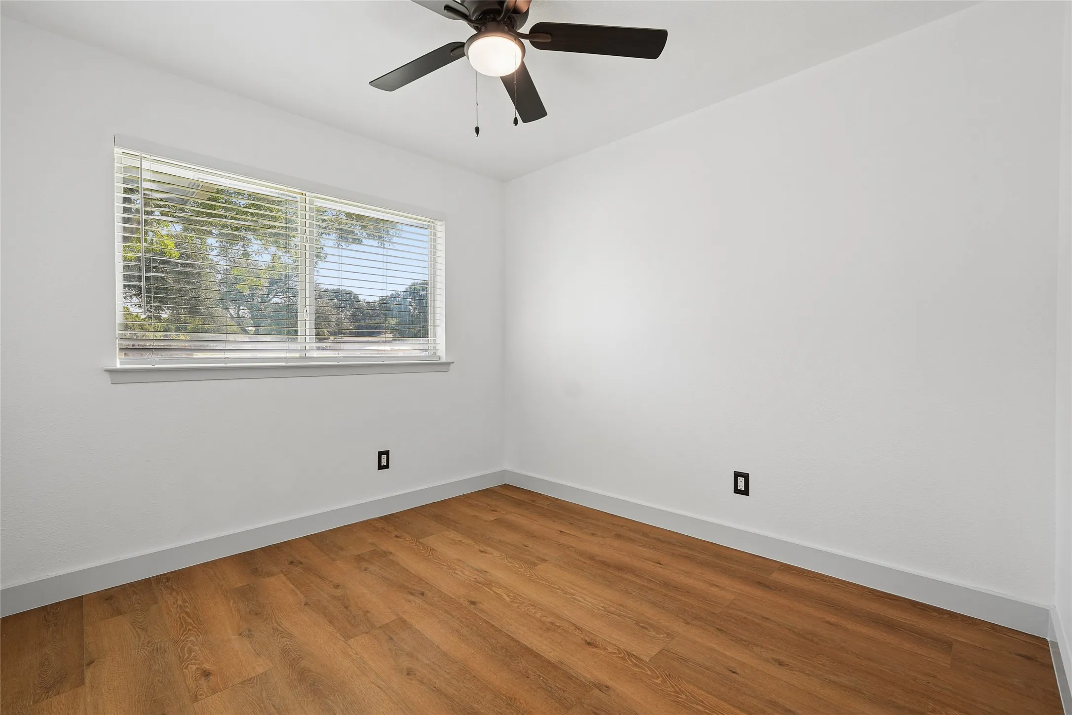 Room featuring wood-finish flooring, a window with horizontal blinds, and a dark bronze ceiling fan with integrated lighting