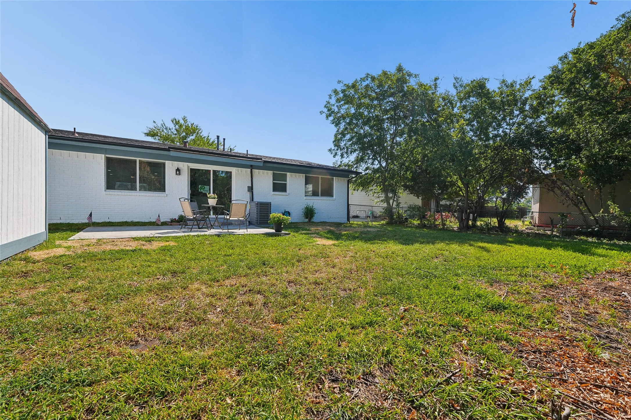 Spacious rear yard featuring a concrete patio, sliding glass door entry, and mature trees along the property line