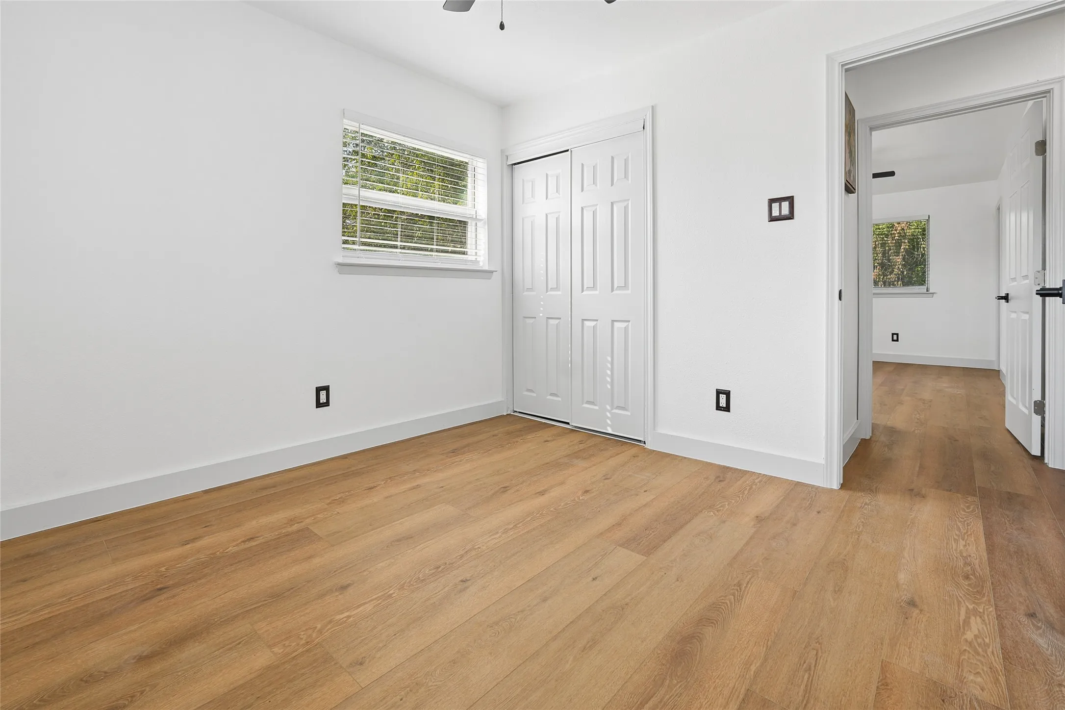 Interior room featuring wood-finish flooring, white walls, and a window with blinds