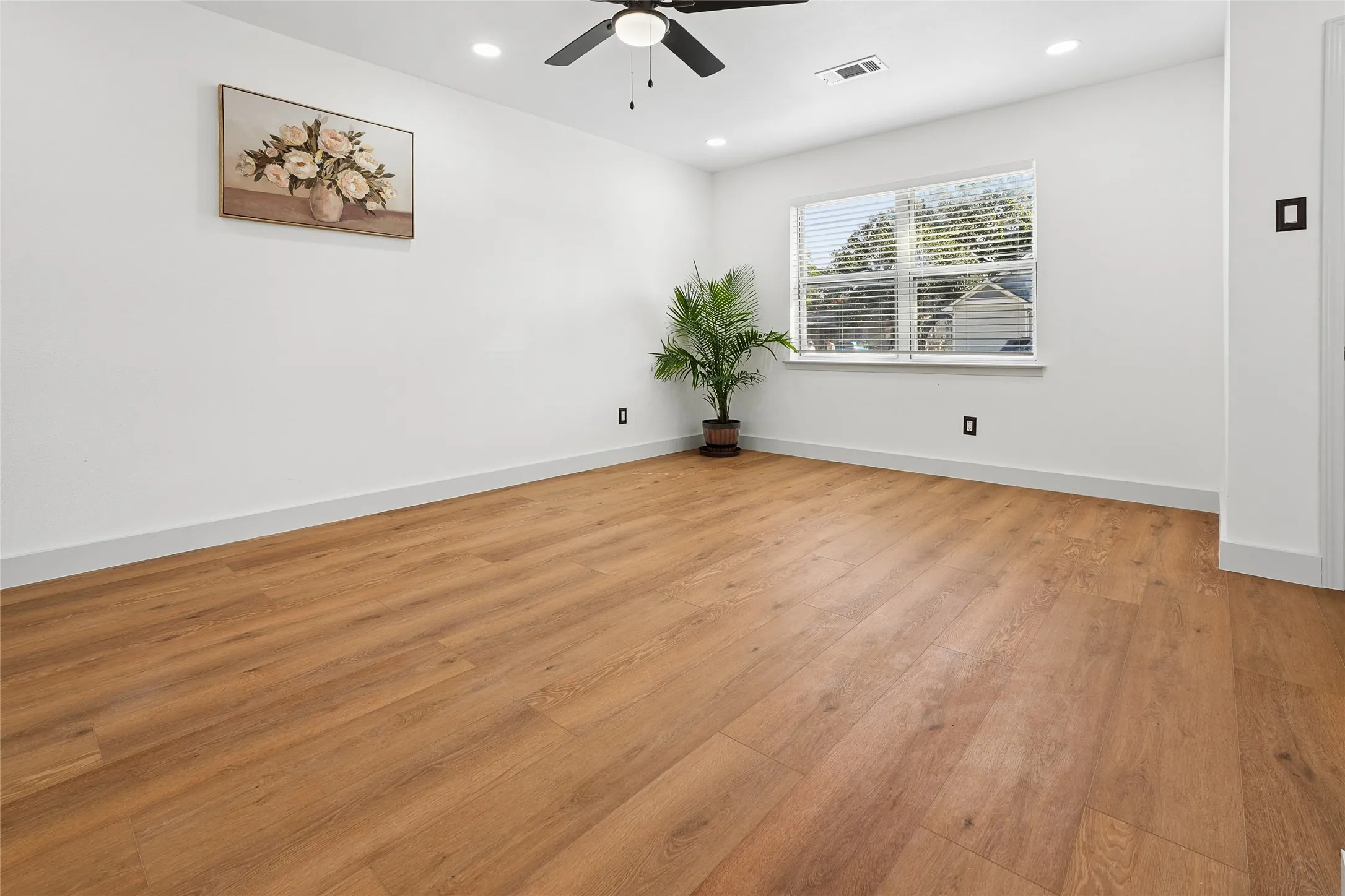 Open room featuring wood-finish flooring, white baseboards, and a window with blinds
