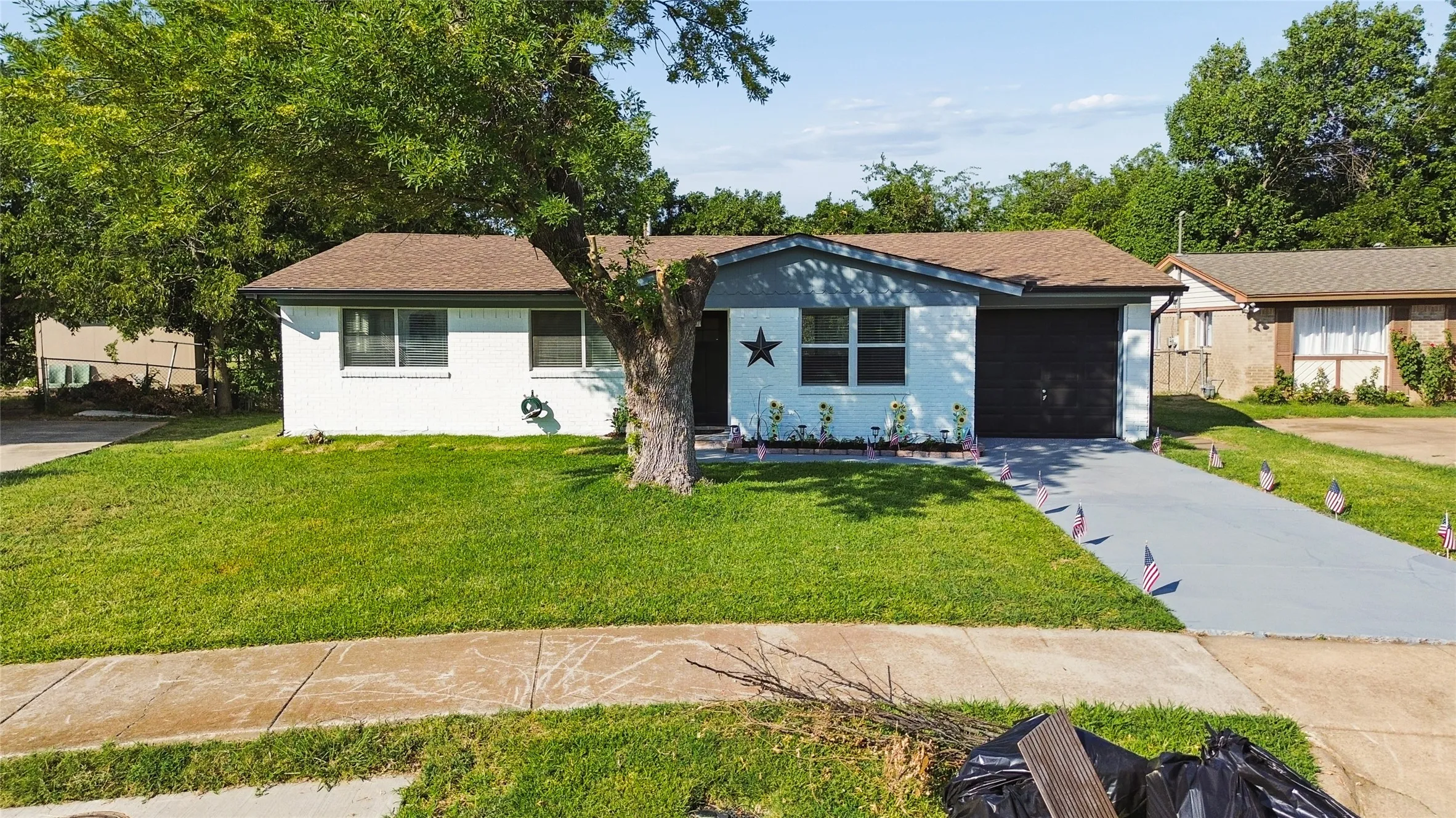 Single-story residence featuring a two-tone exterior, an attached garage, a paved driveway, and a front lawn with mature trees