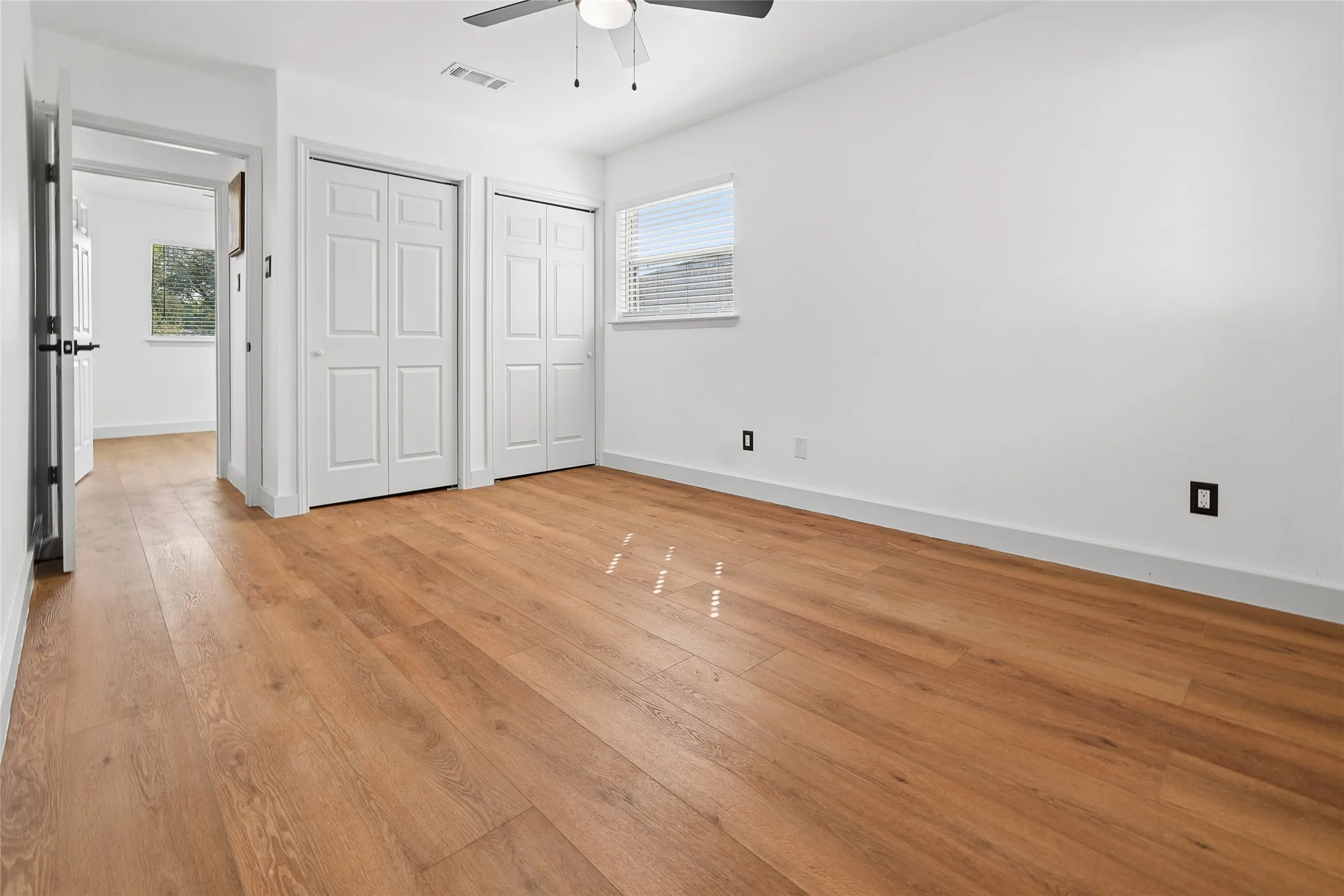 Bright room featuring wood-finish flooring, white walls, and a ceiling fan