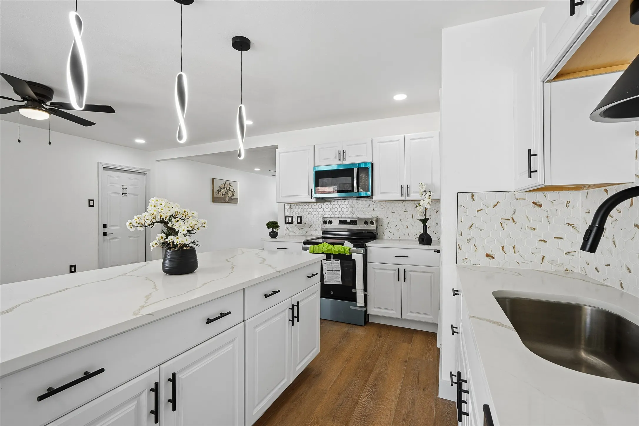 Contemporary kitchen featuring white cabinetry with matte black hardware, white quartz countertops, stainless steel appliances including a built-in microwave, and a large waterfall-edge island