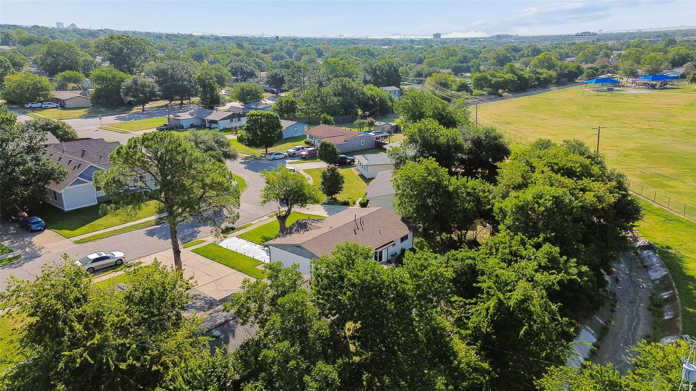Aerial perspective showcasing surrounding properties, mature trees, and nearby green space