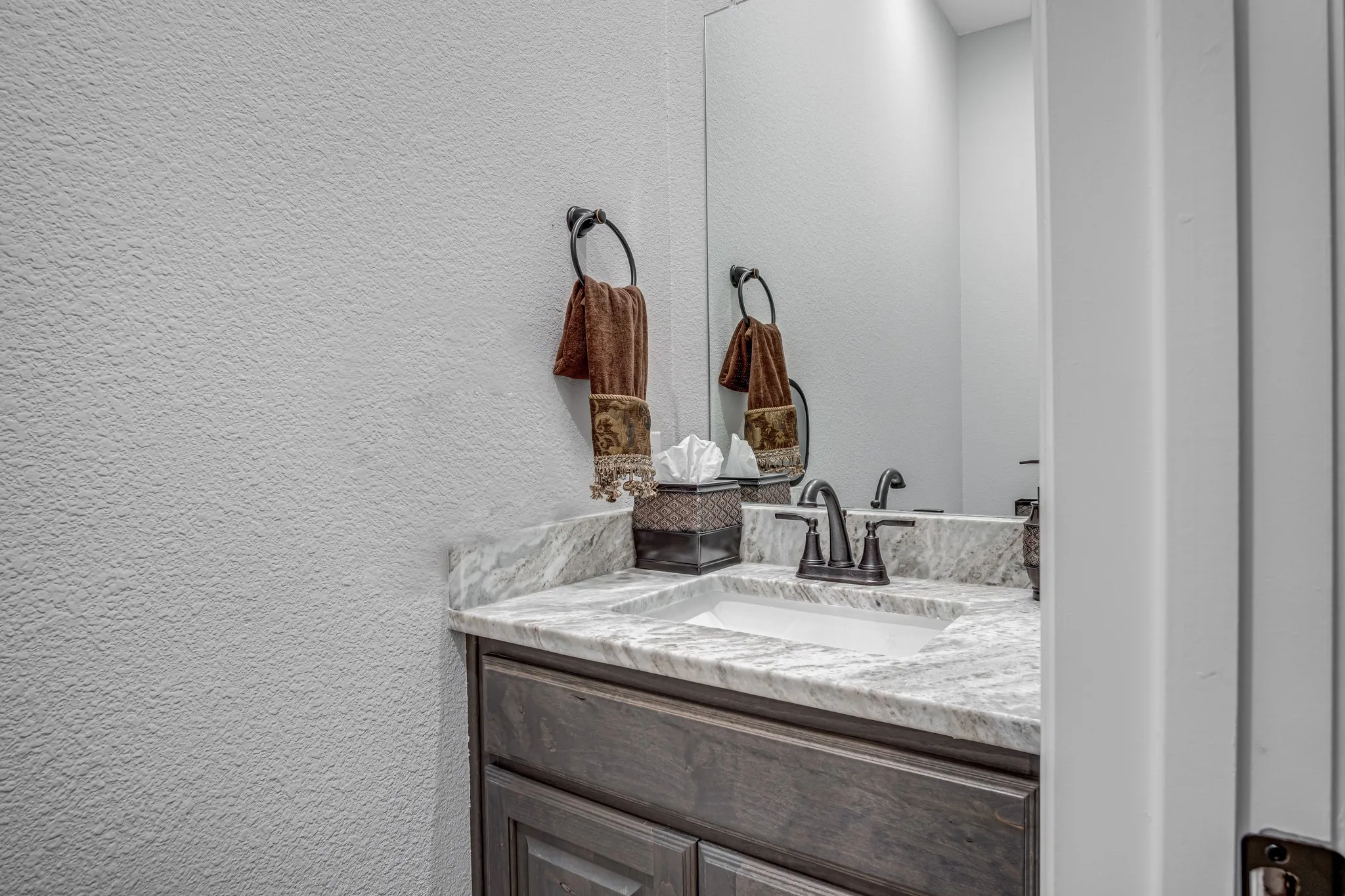 Bathroom vanity featuring a light-toned stone countertop, integrated sink, and dark bronze-finish fixtures