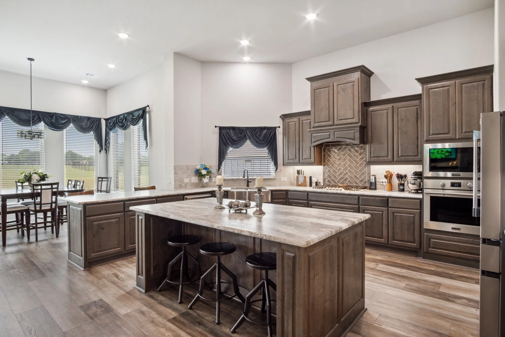 Open-concept kitchen featuring an oversized island with counter seating, wood-finish flooring, recessed lighting, and stainless steel appliances