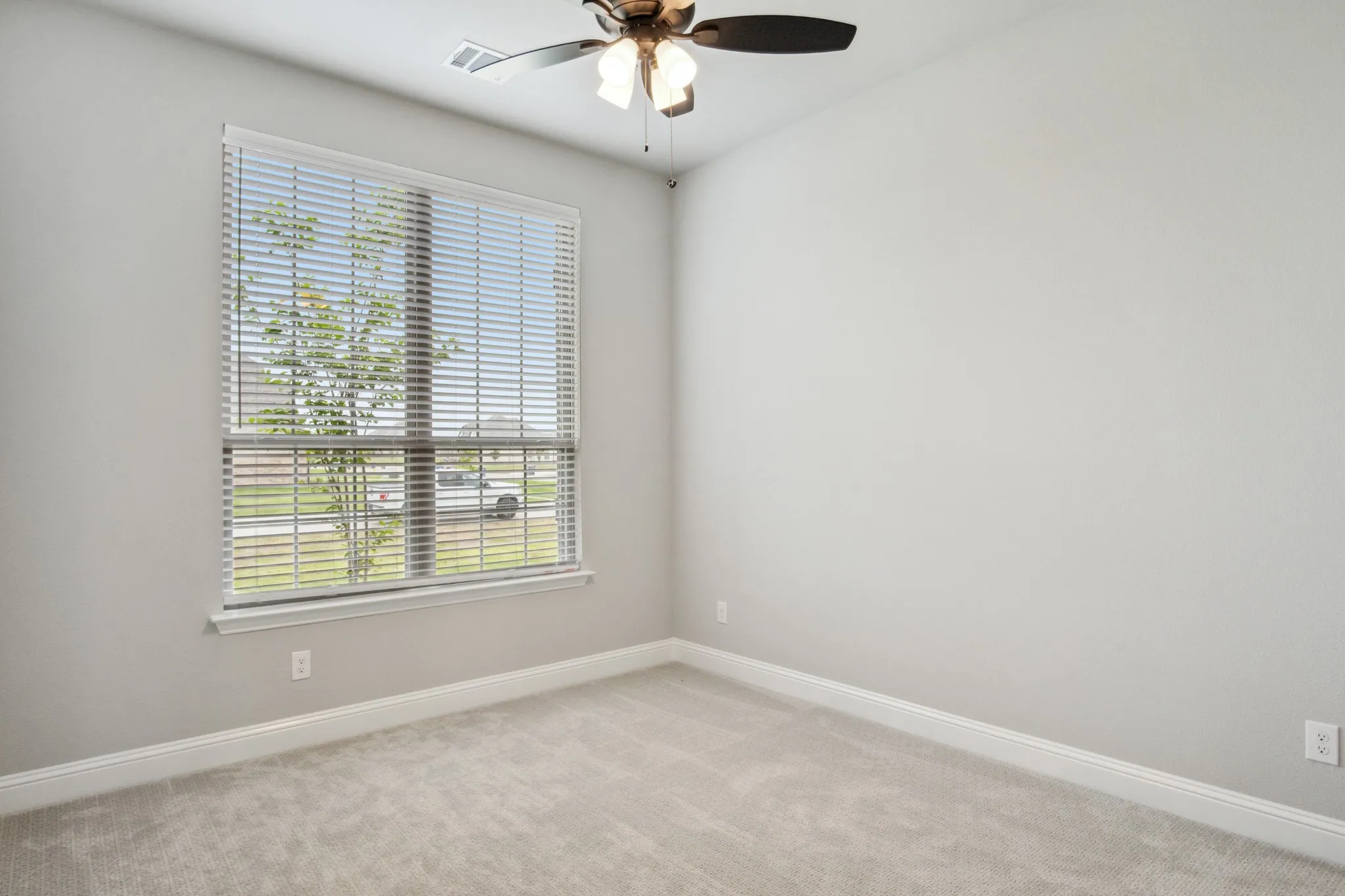 Bright and airy bedroom showcasing neutral carpeting, crisp white walls, and abundant natural light from a large window with plantation shutters