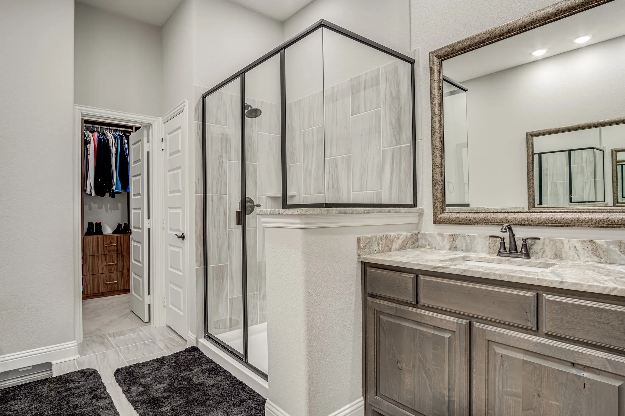Bathroom featuring a glass-enclosed shower with black trim, a vanity with a light-colored countertop, and an ornate framed mirror