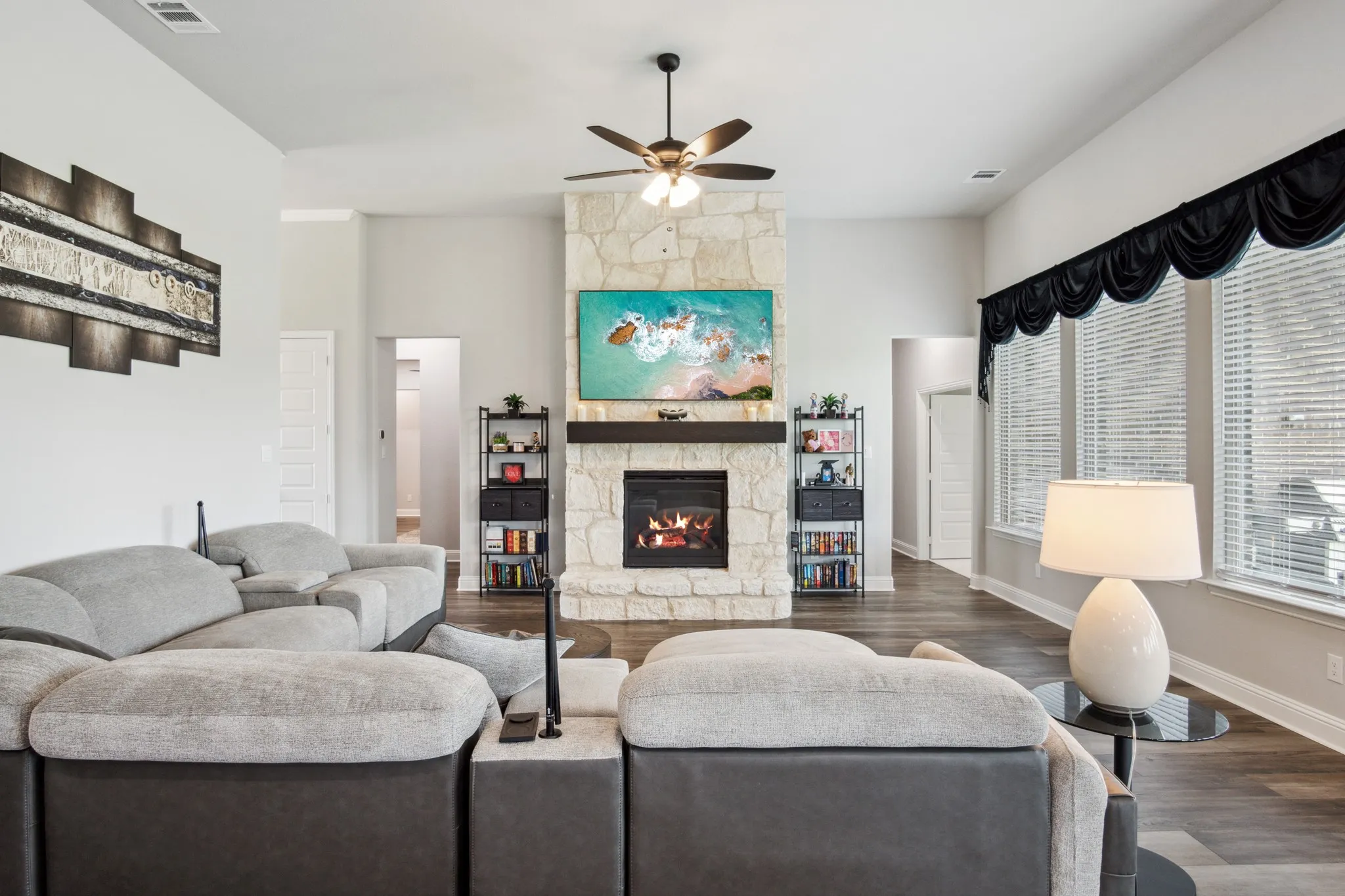 Stone-clad fireplace with a wood mantle and built-in shelving, complemented by high ceilings, wood-finish flooring, and expansive windows