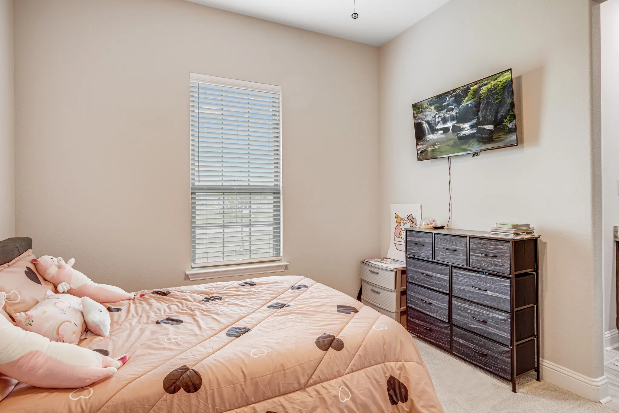 Carpeted room with a single window featuring blinds, off-white wall paint, and a wall-mounted television