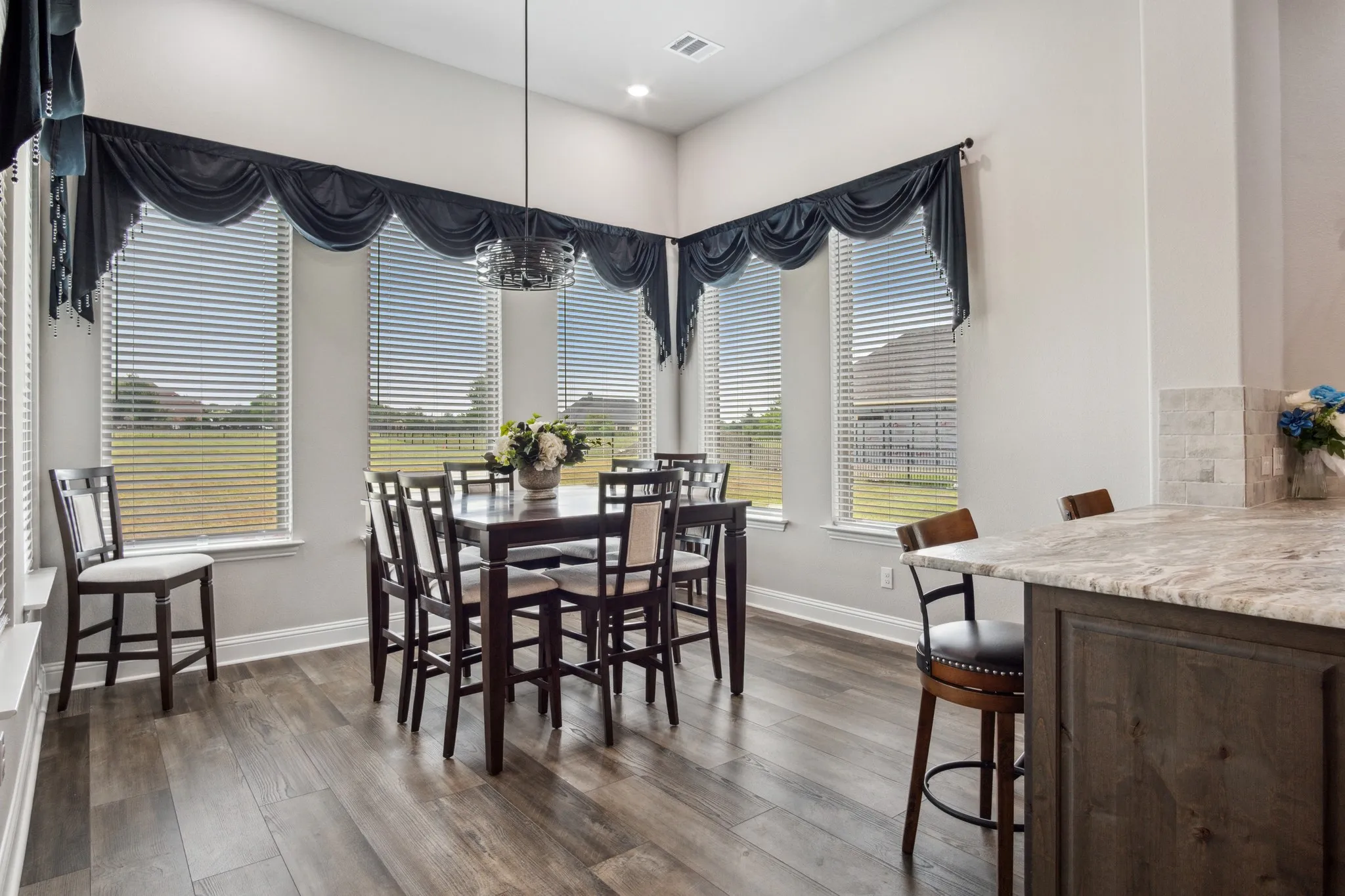 Dining area featuring wood-finish flooring, multiple windows with blinds, a modern chandelier, and a counter-height bar with a granite-style countertop