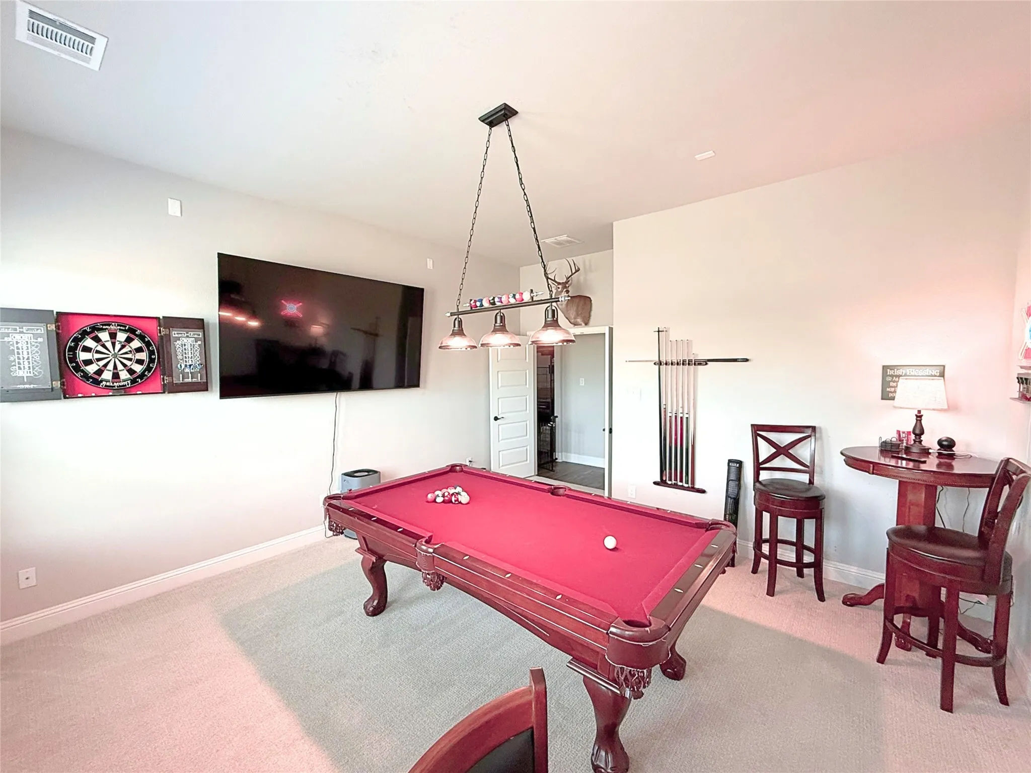 Recreation room featuring a regulation-size pool table with burgundy felt and cue storage, wall-mounted flat-screen television, dartboard with cabinet housing, decorative pendant lighting fixture, and carpeted flooring throughout