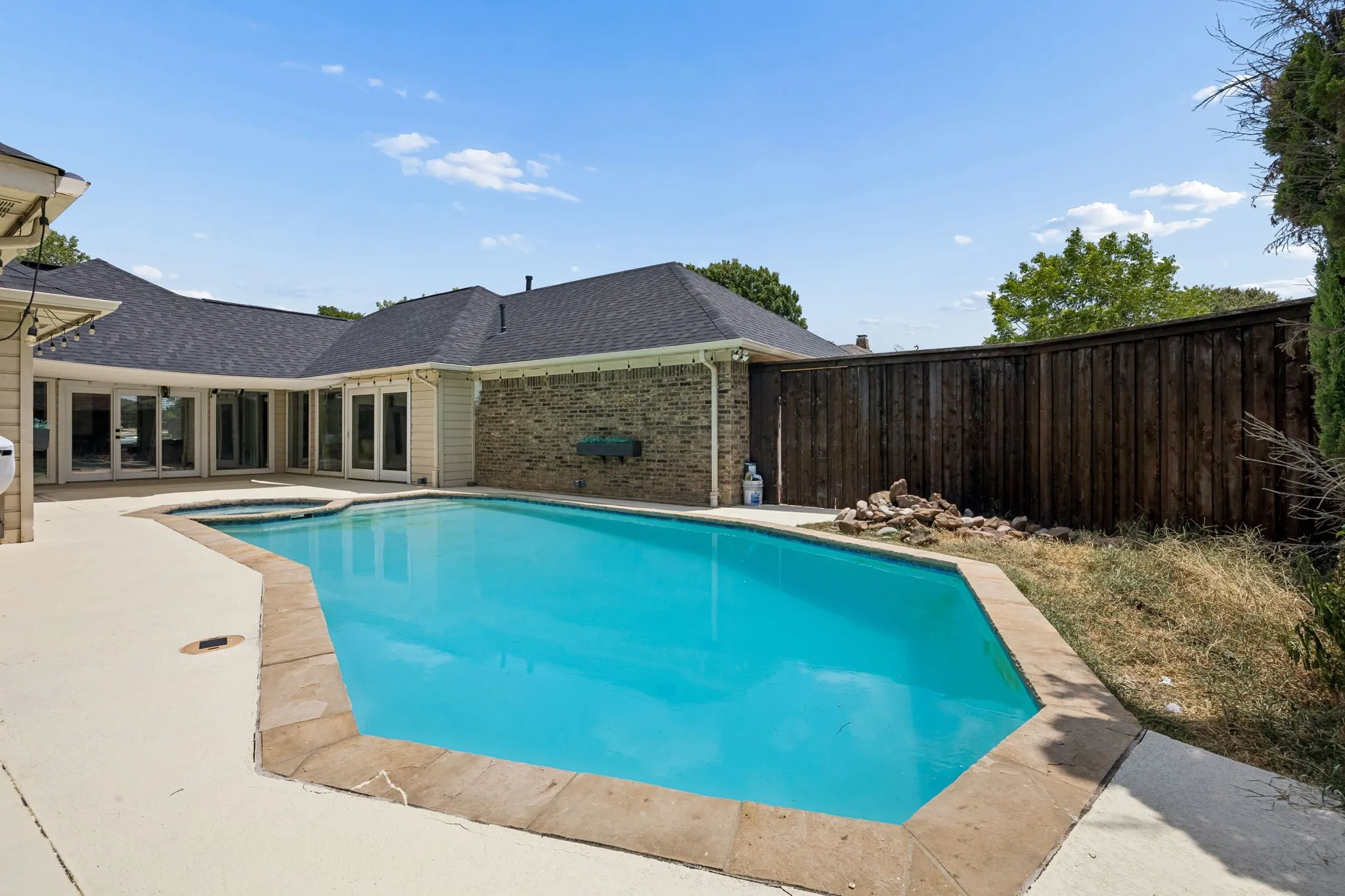 In-ground pool with integrated spa, surrounded by a light-toned concrete patio