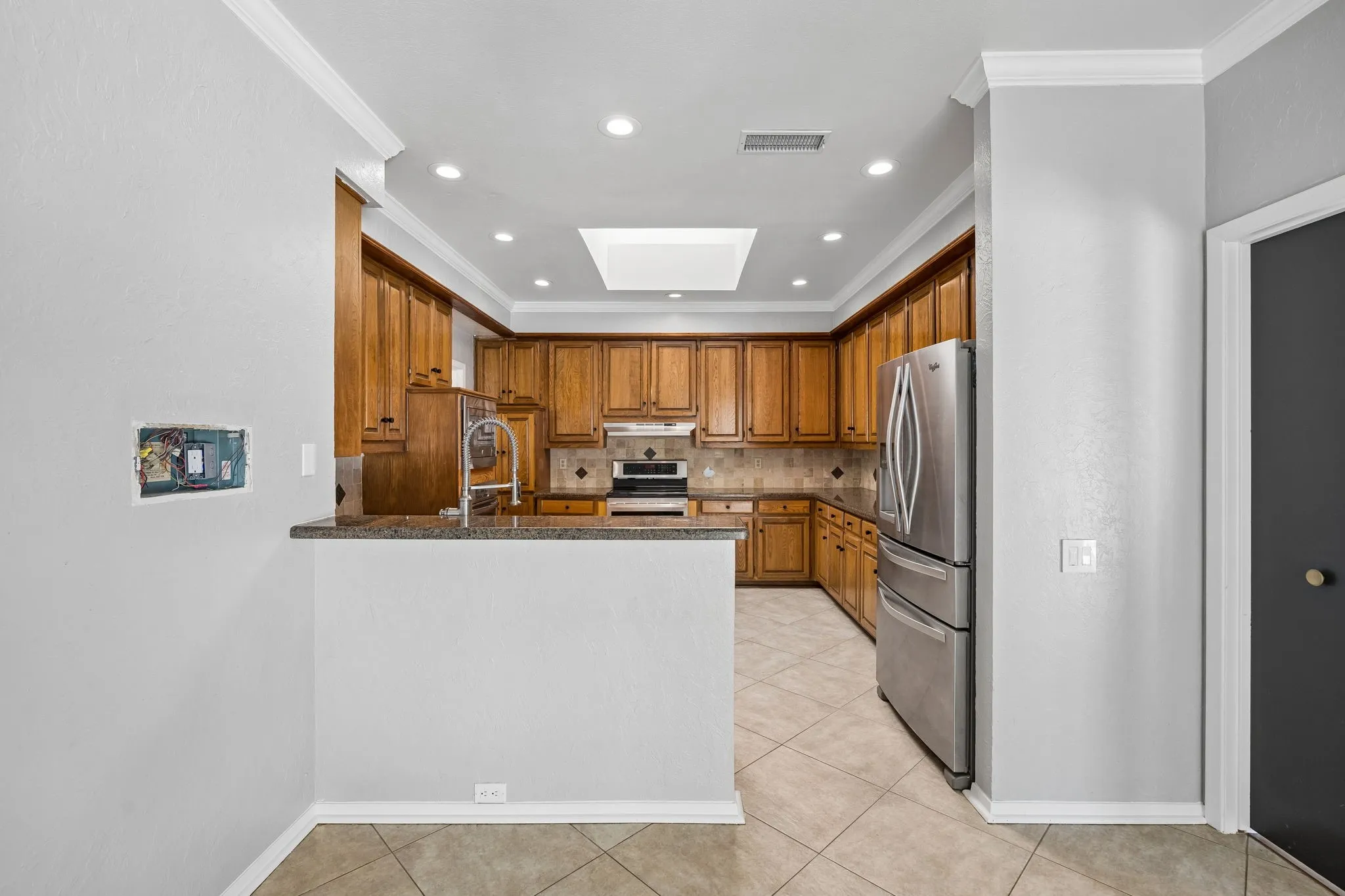 Kitchen featuring wood cabinetry, stainless steel appliances, a tile backsplash, recessed lighting, and a skylight