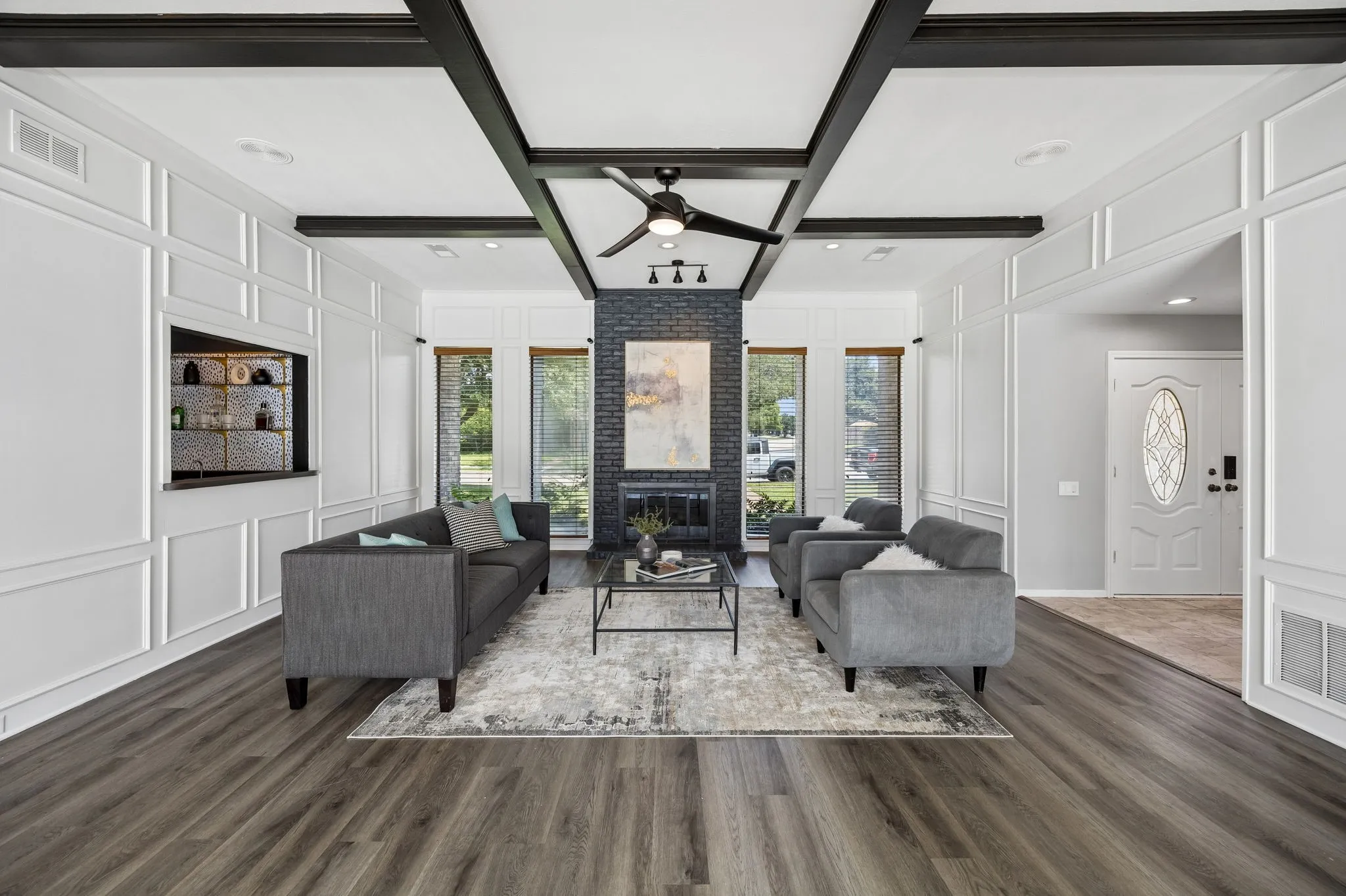 Spacious living area featuring wood-finish flooring, a contemporary fireplace with a stone-finish facade, and a coffered ceiling with dark beams