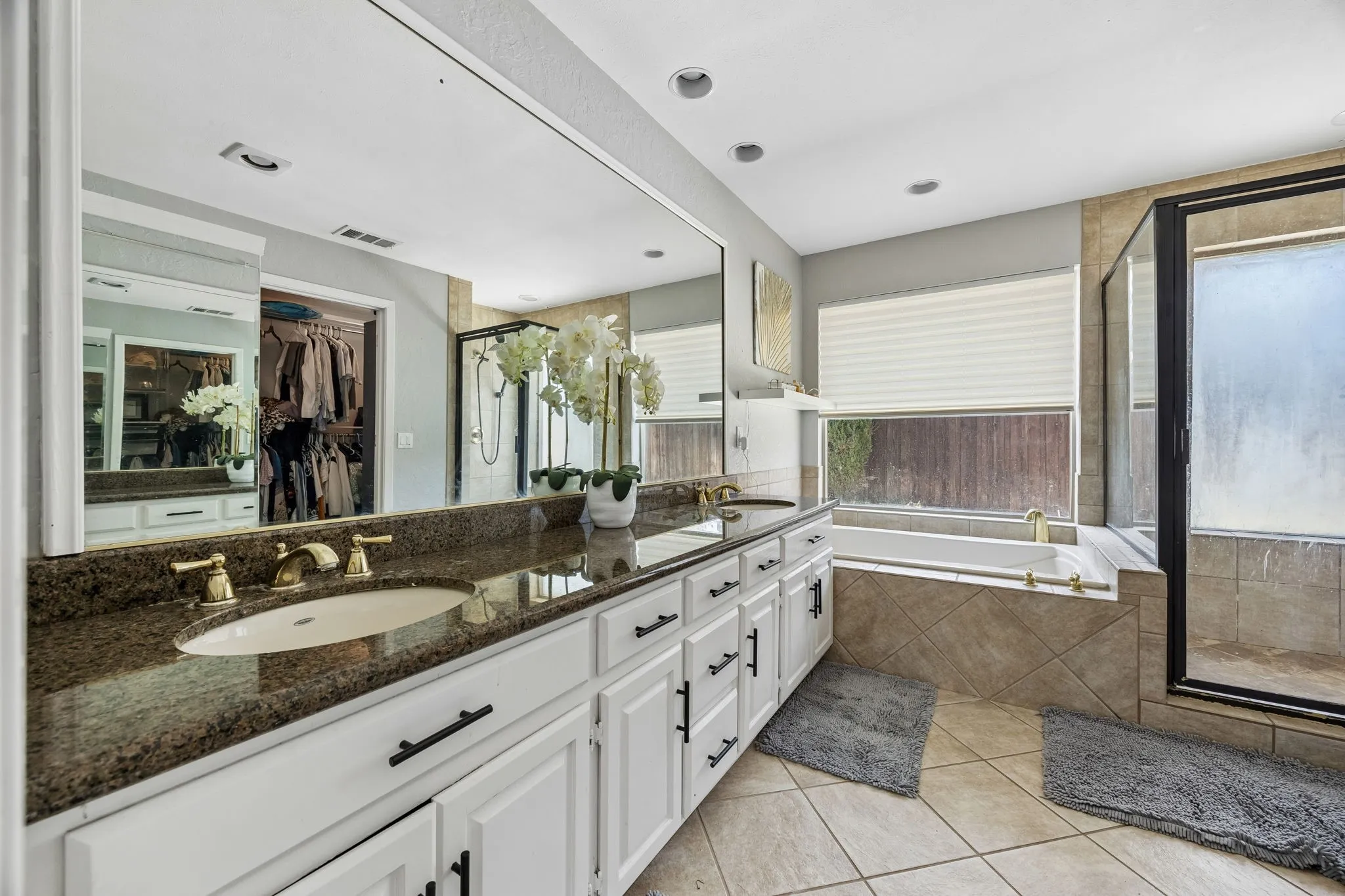 Spa-inspired primary bathroom showcasing dual vanities with granite countertops, white cabinetry with oil-rubbed bronze hardware, and an expansive illuminated mirror