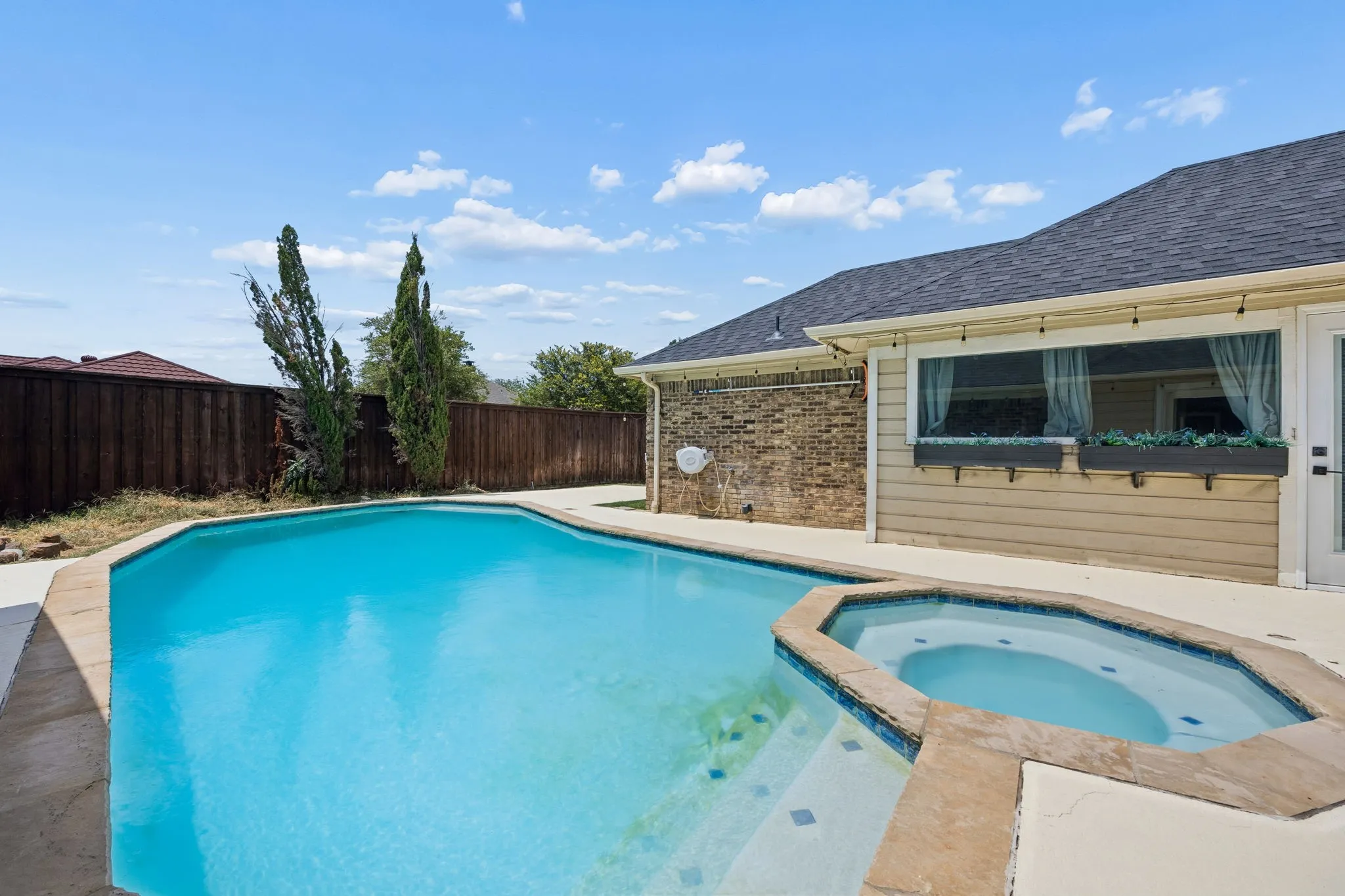Resort-style backyard oasis featuring a sparkling in-ground swimming pool with curved edges, integrated spa tub, and sun deck hardscaping