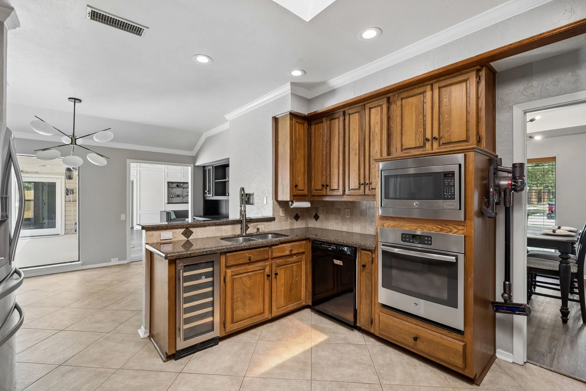 Kitchen featuring wood cabinetry, stainless steel appliances including a built-in microwave and oven, a wine refrigerator, and light-toned tile flooring