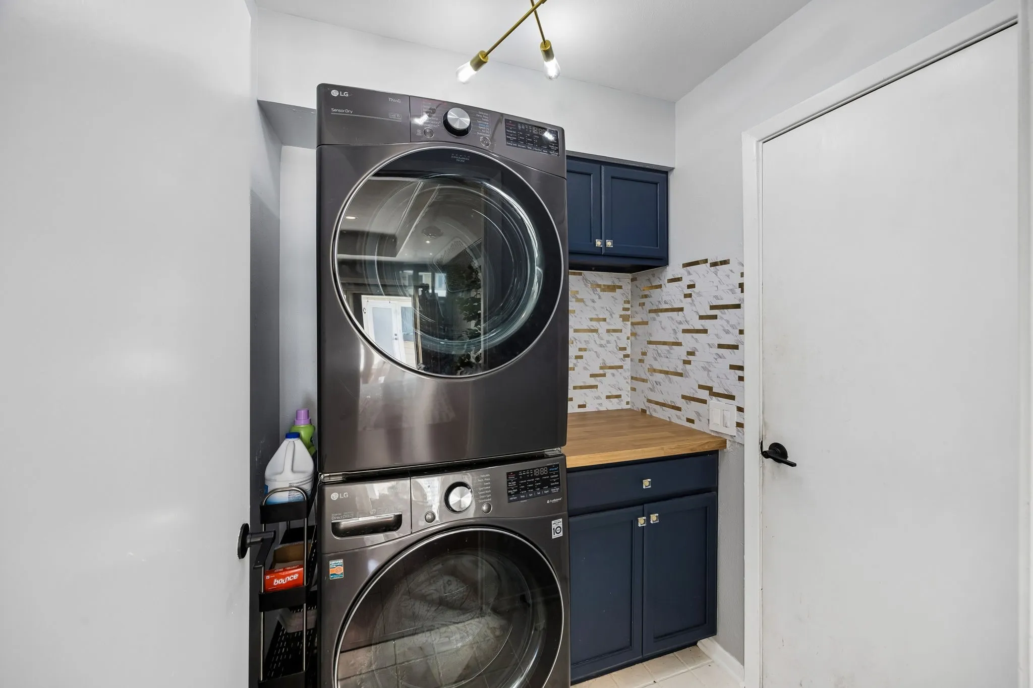 Dedicated laundry area featuring a stacked washer and dryer, dark blue cabinetry, a light wood-finish countertop, and a decorative tile backsplash