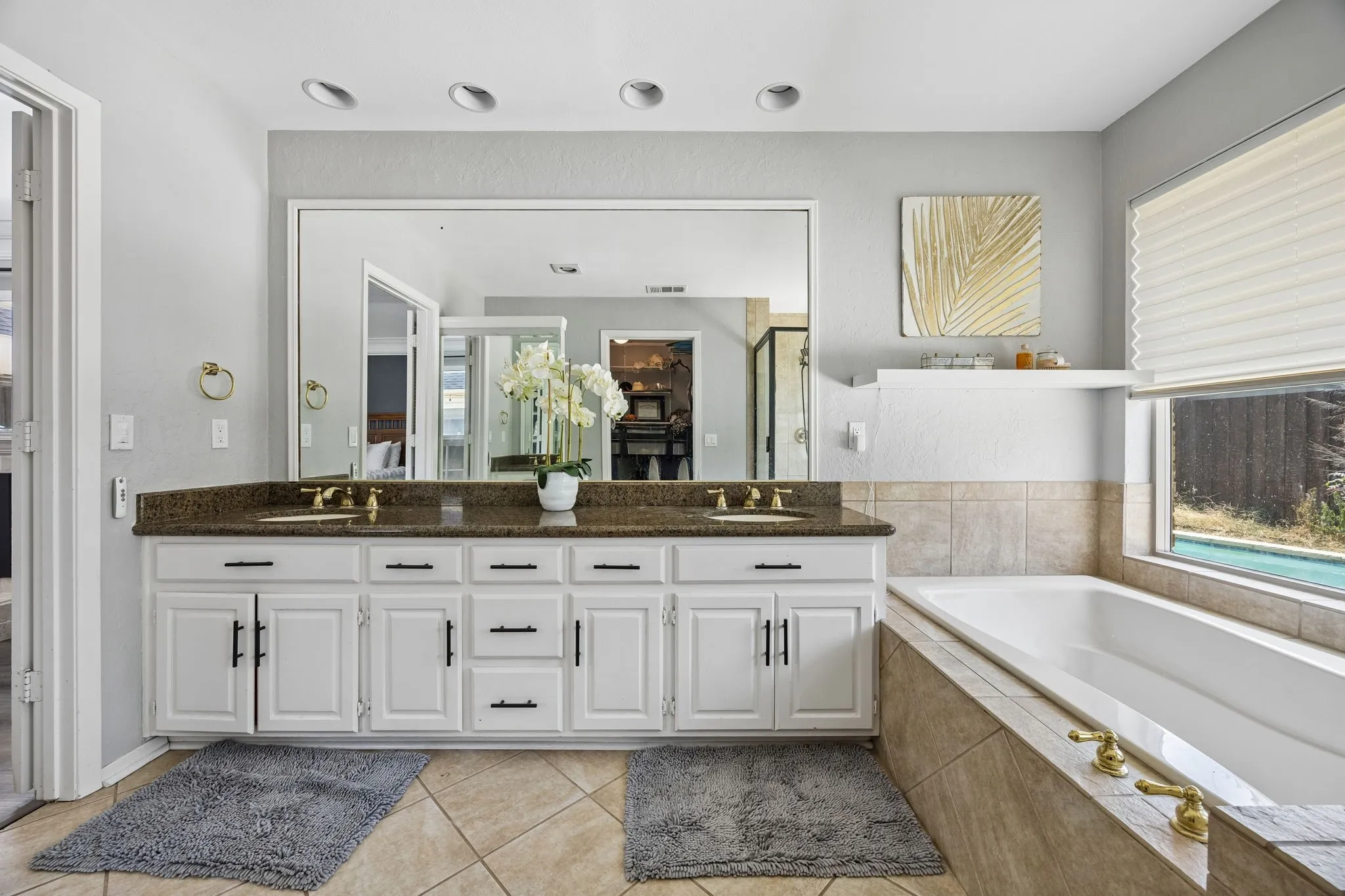 Bathroom featuring a dual vanity with a dark stone countertop, white cabinetry with black hardware, and an integrated soaking tub
