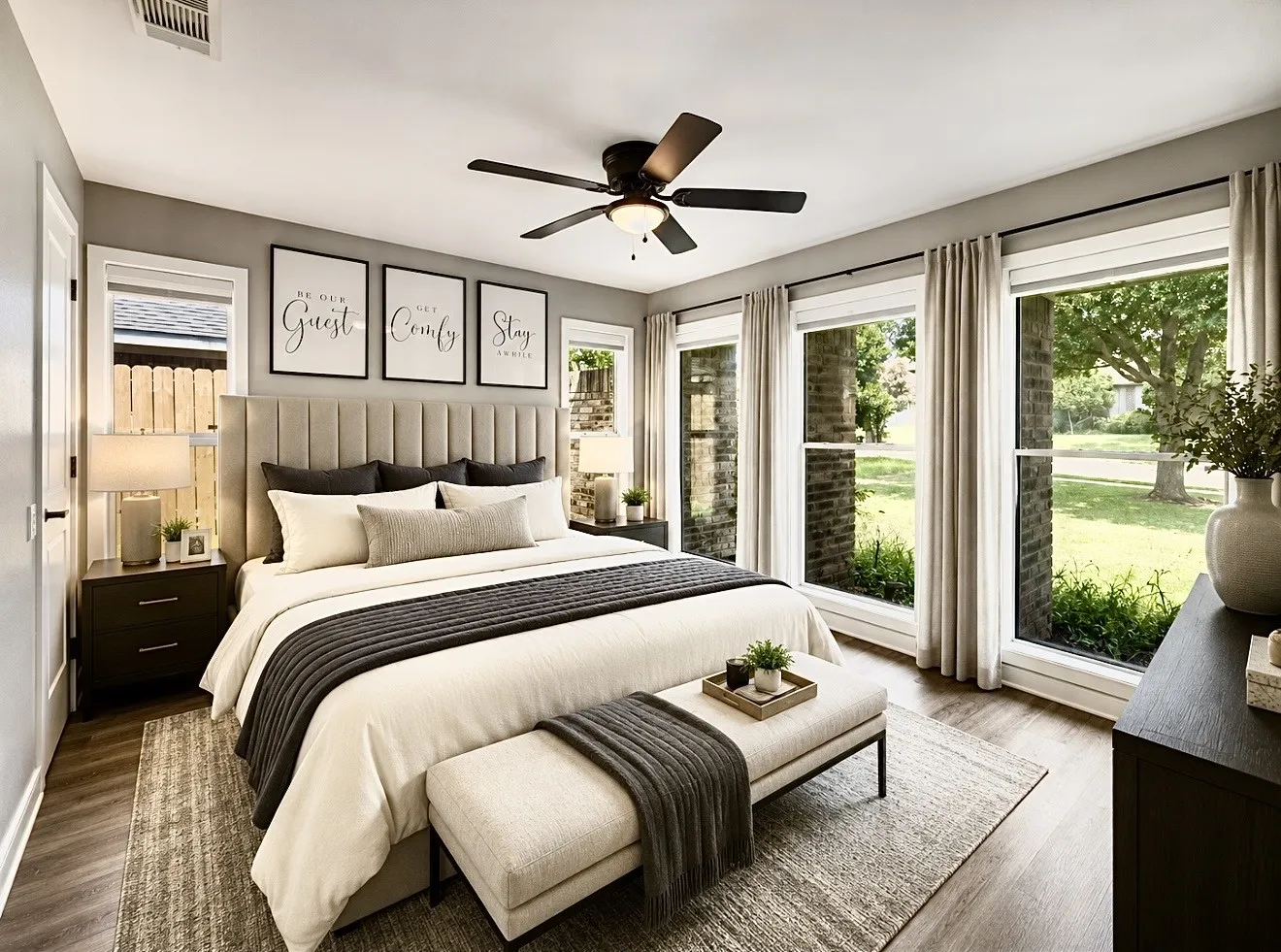 Spacious bedroom featuring wood-finish flooring, a contemporary ceiling fan, and multiple large windows with vertical blinds