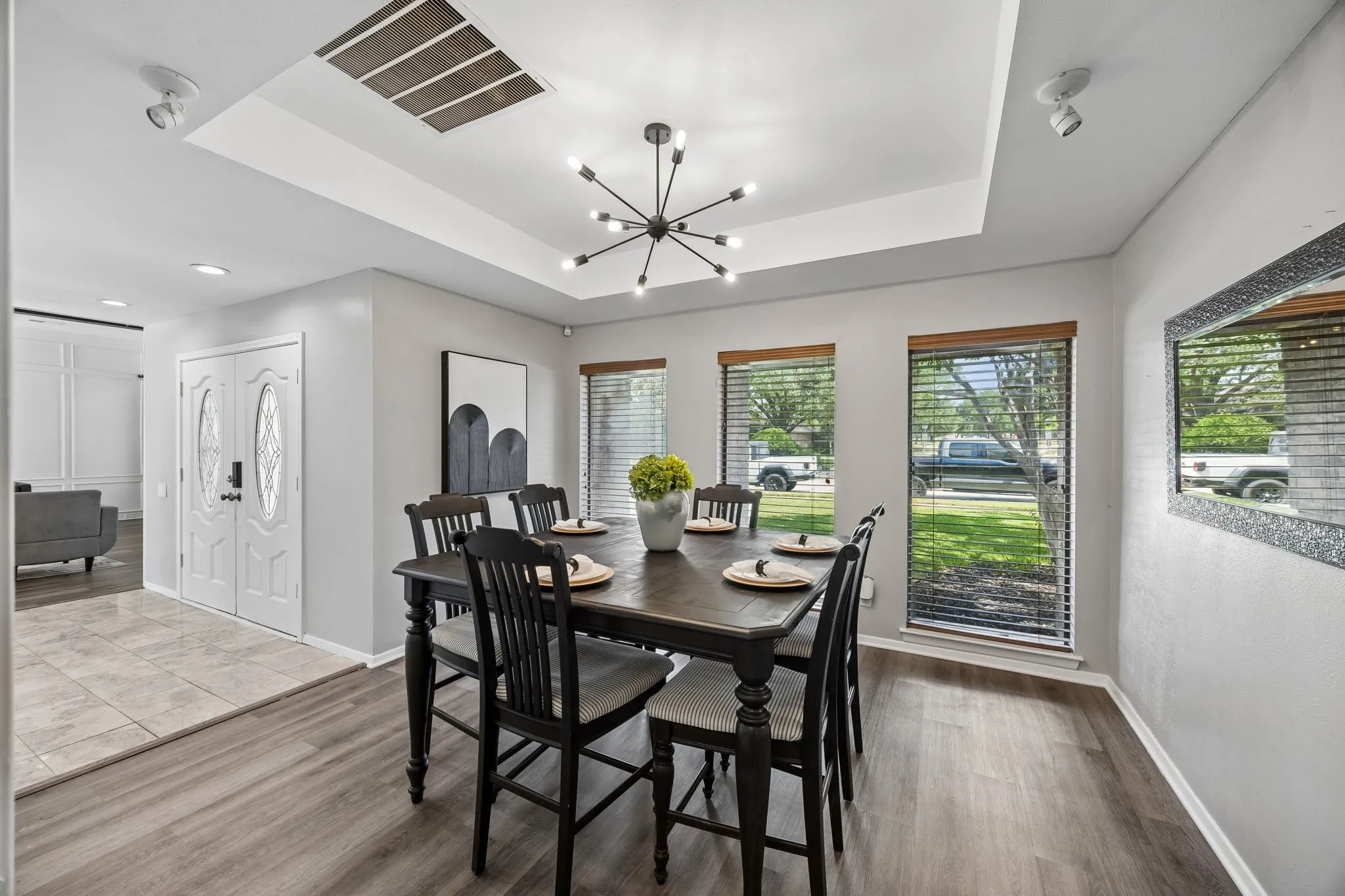 Dining area featuring wood-finish flooring, a tray ceiling with a contemporary light fixture, and multiple windows with wood blinds