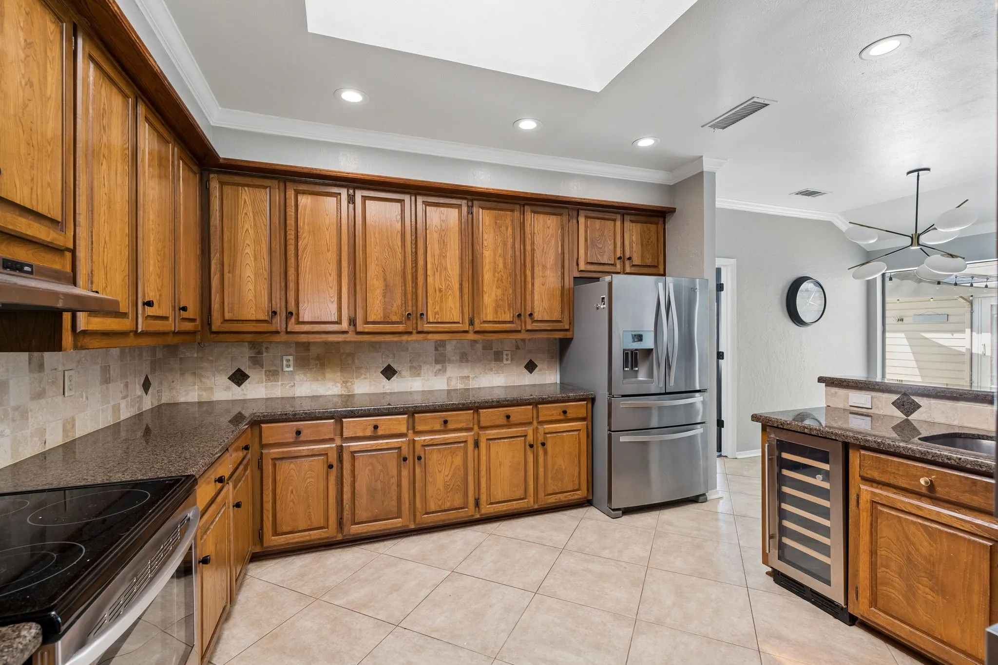 Kitchen featuring extensive wood cabinetry, dark countertops, a tile backsplash with diamond accents, stainless steel appliances, and tile flooring