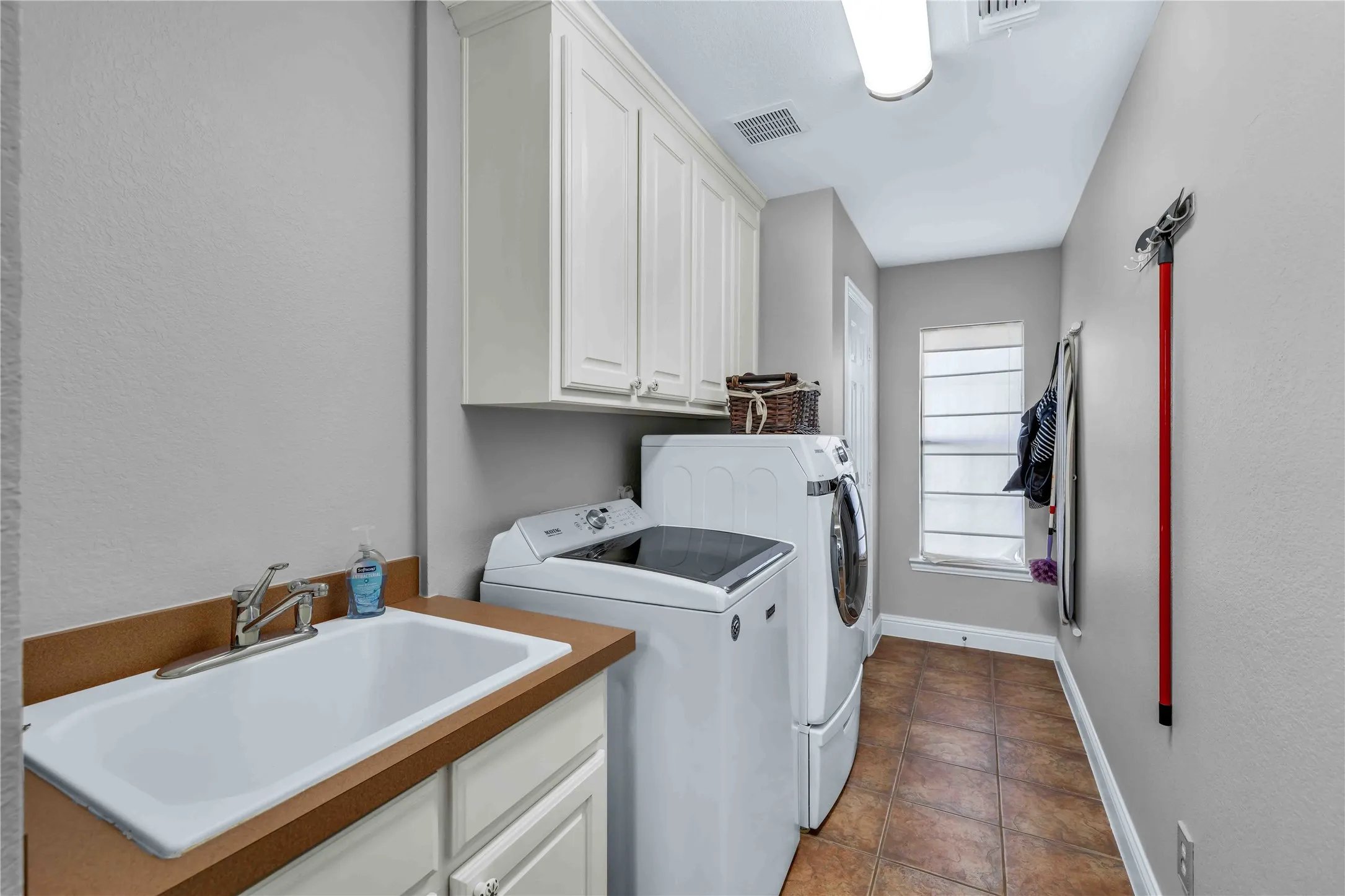 Dedicated utility space featuring a built-in sink with countertop, upper and lower cabinetry, tiled flooring, and a window for natural light