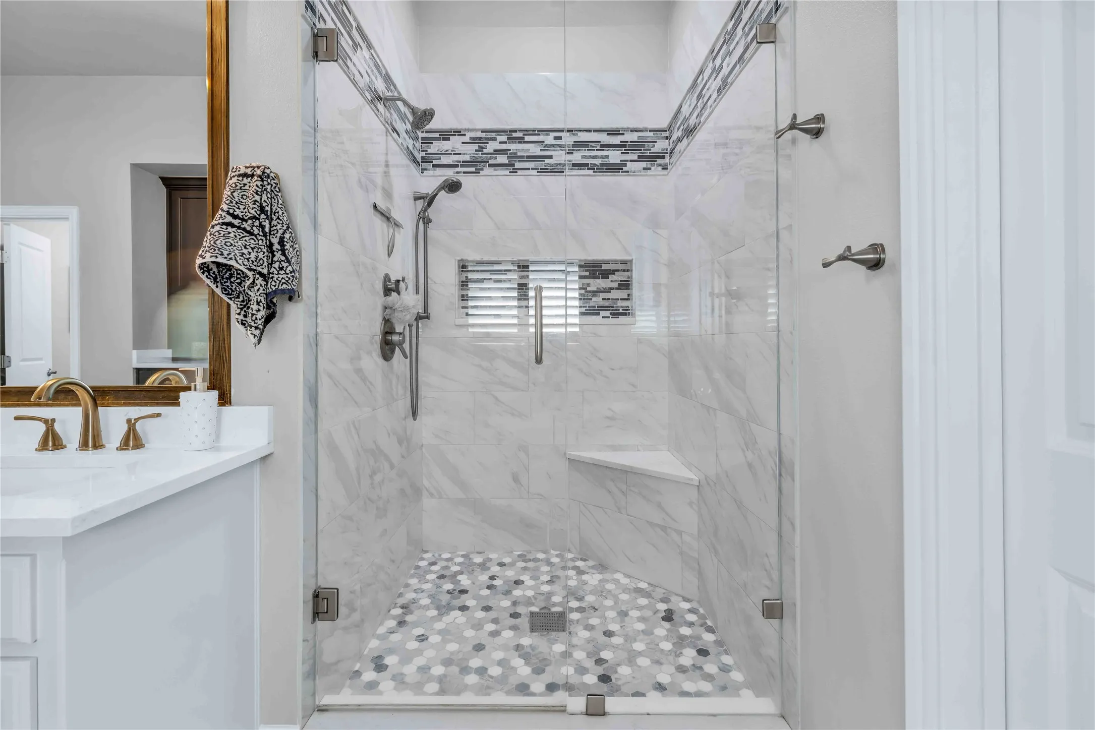 Spacious shower with glass enclosure featuring marble-look wall tiling and mosaic accent band