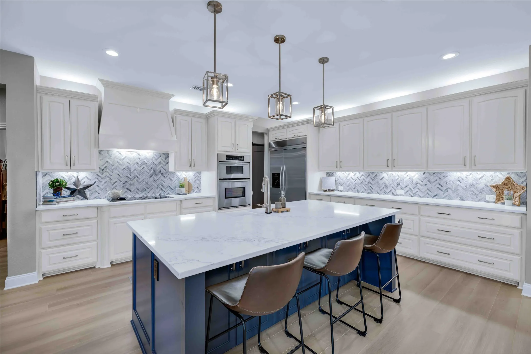 Contemporary kitchen featuring a large central island with seating, white shaker cabinetry, stainless steel appliances, and wood-finish flooring
