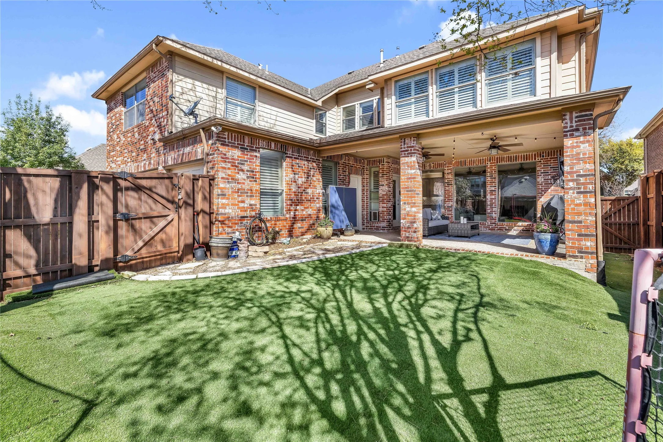 Expansive backyard featuring artificial turf, a covered patio with brick pillars, and ceiling fans