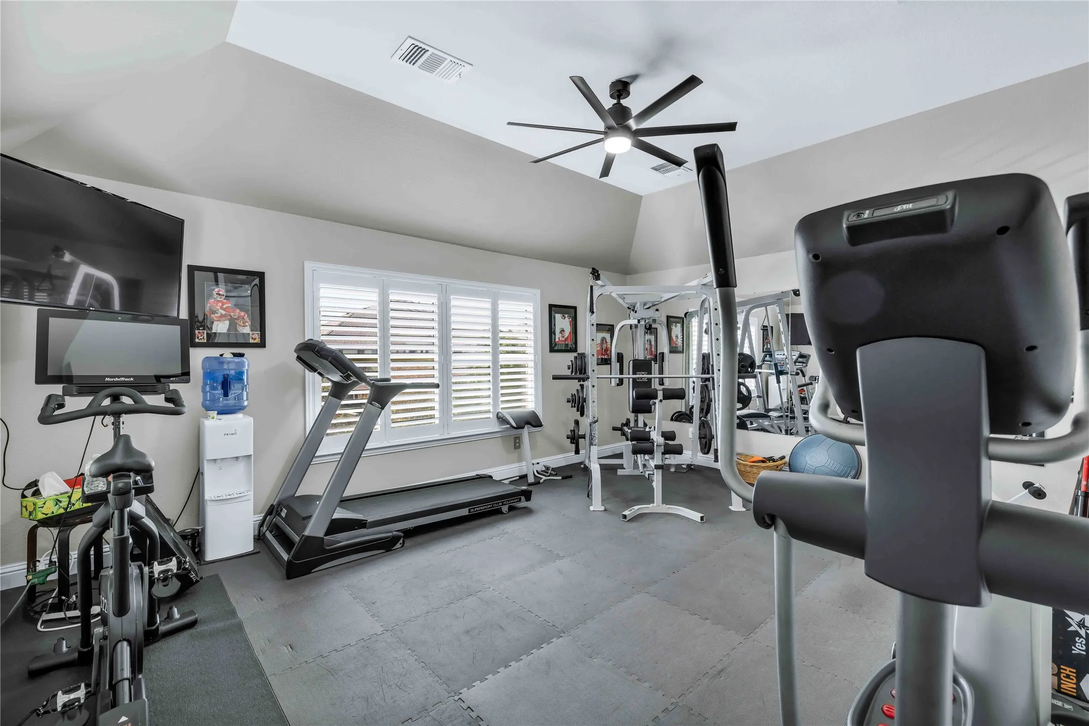 Dedicated room featuring vaulted ceilings, a ceiling fan, window shutters, and resilient flooring