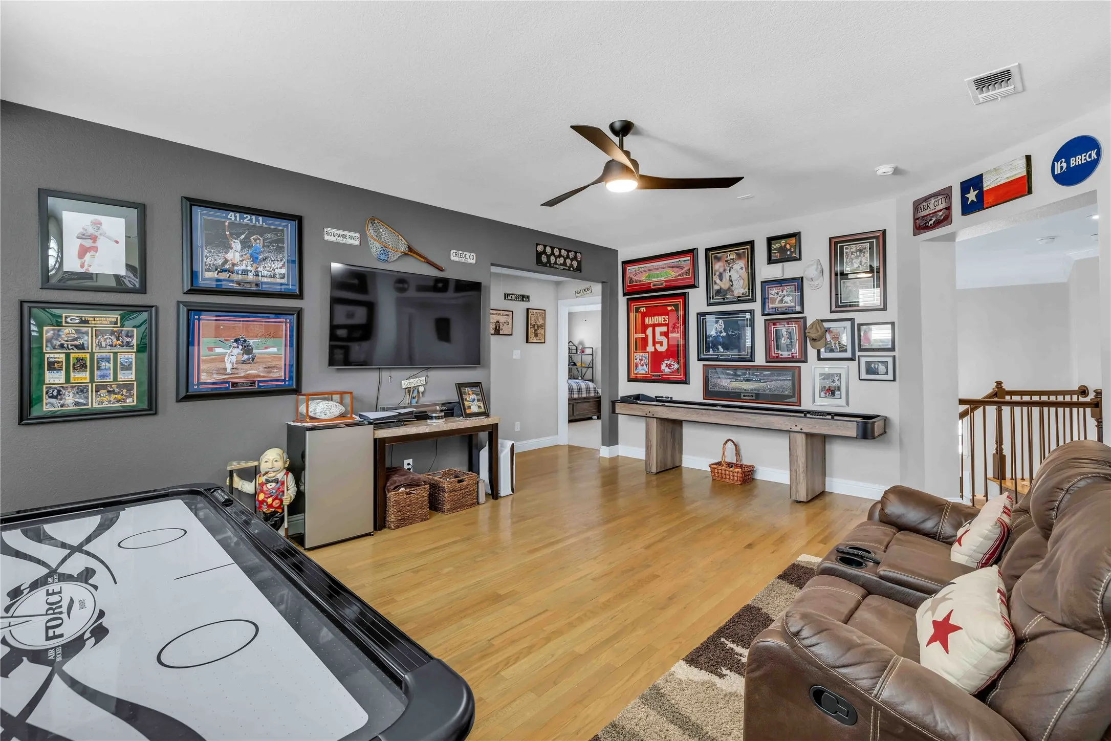 Spacious entertainment area featuring wood-finish flooring, a contemporary ceiling fan, and a built-in console for media